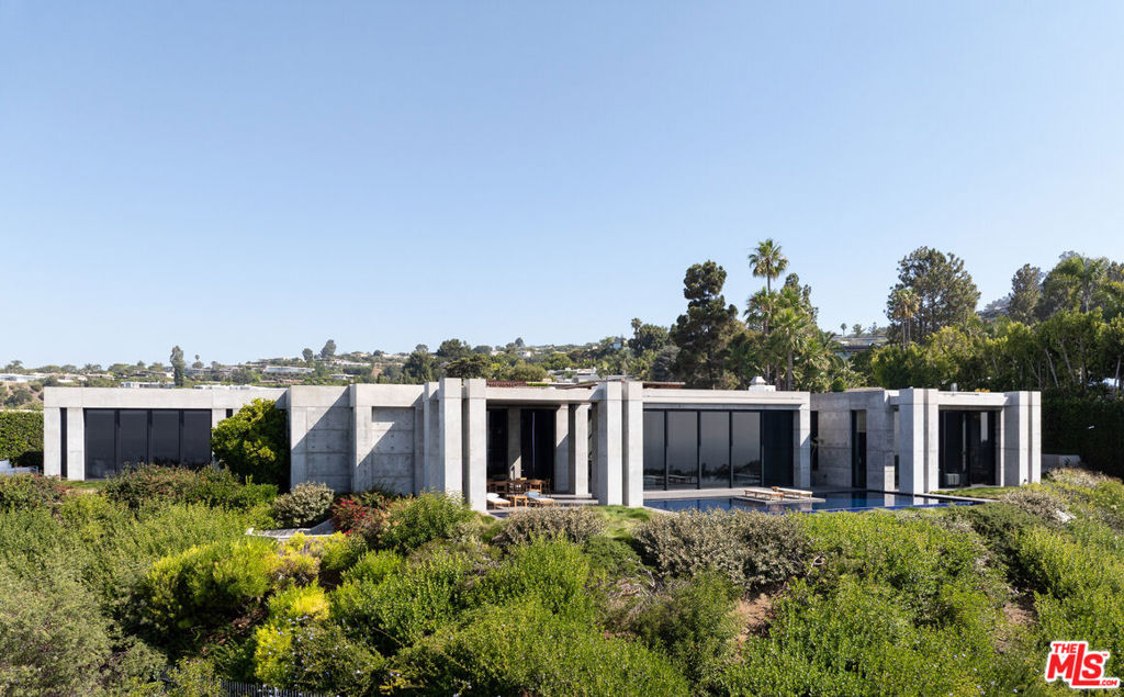 Set at the top of Trousdale, this unparalleled estate is a bold exploration of raw precision, industrial elegance, and sculptural architecture, all while capturing sweeping 180-degree southern views. Designed and built by the acclaimed ID Group, the home centers around a circular motor court enveloped by rhythmic board-formed concrete. Monolithic walls serve as both privacy buffers and dynamic light sculptures, casting dancing shadows from sunrise to dusk. Inside, the architectural intent continues with oversized concrete volumes, perforated metal ceilings, and brushed steel detailing. Framed views of the city and ocean command attention, most dramatically from the main living room, where a retractable glass wall opens to an infinity-edge pool and a horizon that stretches across the Los Angeles skyline. One of the home's most striking features, a fully exposed concept motorcycle, is installed beneath a skylit entry, serving as a dramatic showpiece. Skylights and deep architectural reveals filter daylight through the interiors, creating a constantly shifting interplay of light and shadow. Resort-caliber amenities include a state-of-the-art theater, a spa-inspired primary bath, manicured grounds, walk-in humidor, and meticulously curated one-of-a-kind fixtures. Every element of the home, from its structural form to its bespoke finishes, has been purposefully designed, making 410 Trousdale a truly singular modernist retreat in the heart of Beverly Hills.