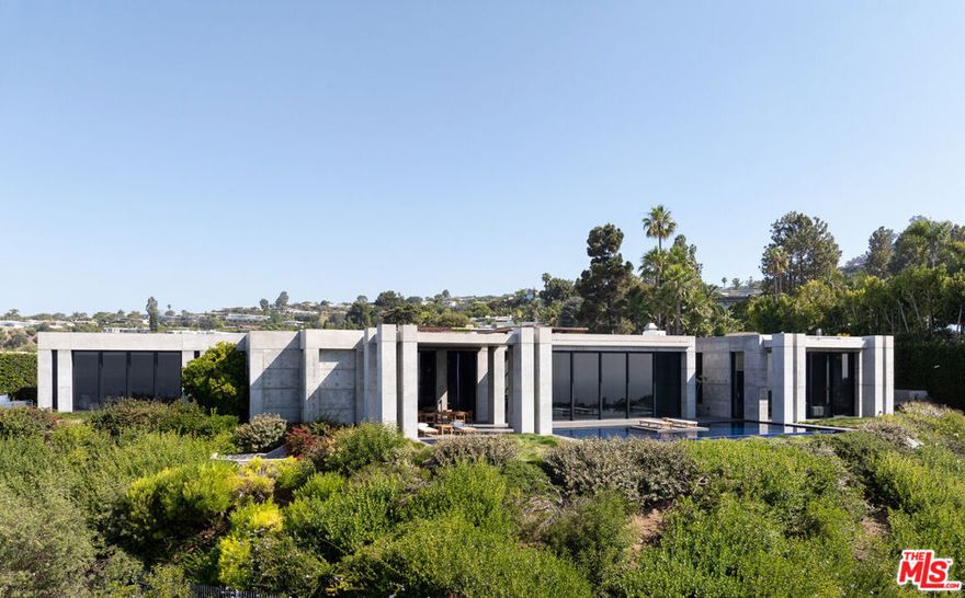 Set at the top of Trousdale, this unparalleled estate is a bold exploration of raw precision, industrial elegance, and sculptural architecture, all while capturing sweeping 180-degree southern views. Designed and built by the acclaimed ID Group, the home centers around a circular motor court enveloped by rhythmic board-formed concrete. Monolithic walls serve as both privacy buffers and dynamic light sculptures, casting dancing shadows from sunrise to dusk. Inside, the architectural intent continues with oversized concrete volumes, perforated metal ceilings, and brushed steel detailing. Framed views of the city and ocean command attention, most dramatically from the main living room, where a retractable glass wall opens to an infinity-edge pool and a horizon that stretches across the Los Angeles skyline. One of the home's most striking features, a fully exposed concept motorcycle, is installed beneath a skylit entry, serving as a dramatic showpiece. Skylights and deep architectural reveals filter daylight through the interiors, creating a constantly shifting interplay of light and shadow. Resort-caliber amenities include a state-of-the-art theater, a spa-inspired primary bath, manicured grounds, walk-in humidor, and meticulously curated one-of-a-kind fixtures. Every element of the home, from its structural form to its bespoke finishes, has been purposefully designed, making 410 Trousdale a truly singular modernist retreat in the heart of Beverly Hills.