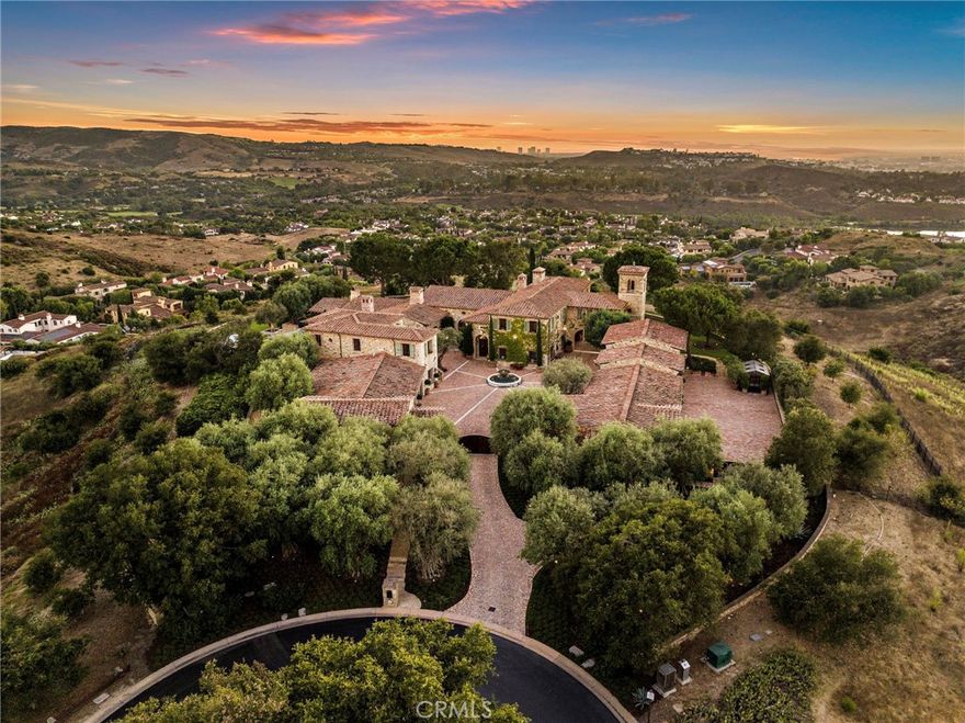 In the prestigious enclave of Shady Canyon, 11 Spike Moss stands as the undeniable crown jewel of the community. This magnificent estate spans 17,660 square feet on a rare 1.33-acre blufftop lot, the largest single lot in the enclave. The residence’s exterior is a masterful display of timeless design with Romanesque thick stone walls and reclaimed Tuscan terra cotta brick and roof tiles, while the estate’s pièce de résistance is the awe-inspiring operating 35-foot stone bell tower, crowned with an exquisite Italian bronze bell. Entering the estate through its gated driveway sends one back in time. Upon entering the grand foyer, the sense of another era remains, as you are greeted with soaring fresco-painted ceilings and an opulent Carrera marble stairway that ascends to the private primary suite. The assembly room, with its soaring ceilings and grand fireplace, sets the stage for sublime gatherings as it melds with the dining room's 20-person antique table and authentic main chef’s kitchen and secondary catering kitchen. The primary suite is an inviting and restful retreat, featuring a reclaimed Tuscan fireplace, a hand-carved stone bathtub, and a private fitness suite. The separate family wing ensures comfort and privacy with four additional bedrooms, four bathrooms, and a private kitchenette. The lower level is an unparalleled realm of entertainment and leisure, transporting you back in time with each step down the stone and brick-clad stairway. Emotions strengthen as you enter a subterranean world with brick-clad walls and groin vault ceilings, and a wine tasting room. Adjacent is the Tuscan cistern-style game room, illuminated by a glass skylight, same as the wine tasting room and the 2,500-bottle wine cellar. A 150-inch screen theater and performance stage delivers an immersive entertainment experience, while the Taverna, with a stylish bar, epitomizes refined relaxation. Outdoor entertainment options are not ignored with a 48-foot infinity pool and private spa, offering a sunny sanctuary of unparalleled peace and indulgence. The meticulously curated grounds feature a full-size bocce ball court, a pizza oven, and a cozy fire pit, all surrounded by manicured landscapes. A professional workshop, three-car garage and six-car “auto barn”, bookend the entry courtyard. Located within minutes of the best beaches, dining, shopping, top schools, and transportation hubs, this estate is a statement of unparalleled style embodying the pinnacle of refined living.