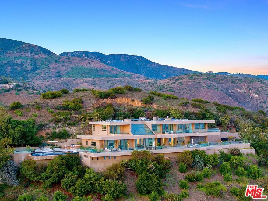 Perched atop the coveted Winding Way in Malibu and spanning approximately 15.5 acres, this architectural masterpiece by acclaimed designer Michael E. Barsocchini offers a rare blend of contemporary elegance and breathtaking natural beauty. With commanding, unobstructed views that sweep from Palos Verdes to Point Mugu, the residence is a sanctuary of coastal luxury. Beyond the second gated entry, a dramatic double-height foyer welcomes you into a striking great room, where a sleek fireplace, retractable glass walls, and honed travertine floors harmonize against an awe-inspiring ocean backdrop. The open-concept layout effortlessly connects the living room, dining area, chef's kitchen, and media lounge each space extending seamlessly onto a sweeping deck that spans the length of the home.A sculptural floating walkway leads to the serene master suite, a private retreat featuring a fireplace, lavish spa-inspired bath, dedicated exercise/yoga studio, custom walk-in closet, office, and a secluded ocean-view deck. Three additional en-suite bedrooms, each framing panoramic views of the Pacific, offer exceptional comfort and privacy. Outdoors, a manicured lawn surrounds the infinity-edge pool, spa, and a fully equipped barbecue pavilion perfect for entertaining. Beyond the pool, scenic trails wind through the upper acreage, inviting peaceful immersion in nature. Witness unforgettable sunsets from this singular designer estate, a jewel in the Malibu hills.