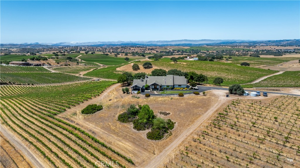 Perched on a scenic knoll with sweeping 360-degree views, this remarkable 80 +/- acre estate offers exceptional privacy, space and timeless craftsmanship in the heart of the Central Coast. The custom-built main residence, completed in 1999, spans approximately 4,649 +/- sf and showcases quality wood-frame construction, stucco siding and a concrete tile roof. Inside, the 4 BD and 3.5 BA are thoughtfully arranged for both comfort and functionality. The dramatic great room is a true centerpiece, featuring vaulted ceilings with exposed oak beams, a floor-to-ceiling gas fireplace, and a wall of windows framing panoramic vistas. Designed for both everyday living and grand entertaining, the home also offers a formal dining area, a wet bar, a casual dining nook with built-in oak hutch and desk, and a well-appointed office with custom cabinetry.
The chef’s kitchen blends style and practicality with Corian countertops, a cooking island with bar seating, custom oak cabinetry, built-in refrigerator, and double convection/conventional ovens. The luxurious primary suite is a private retreat with dual walk-in closets, a spa-inspired bath with Jacuzzi tub, separate shower and vanity island—plus direct access to a Trex deck with a 220V hookup for a hot tub. A separate guest wing includes three additional bedrooms, one with an en-suite bath. Outdoor entertaining is elevated with a covered kitchen area complete with built-in BBQ, sink and seating area overlooking the rolling landscape.
A detached 1,278 +/- sf secondary residence, built in 2006, features 3 BD, 2 BA, and comfortable living spaces—ideal for guests, extended family or on-site staff. A versatile 1,200 +/- sf metal shop with 14-foot eaves, dual roll-up doors and 220V single-phase power offers abundant space for projects and storage.
Outdoors, entertain with a covered kitchen, built-in BBQ, and lush landscaping. The property includes 71± acres of vineyard with 9± acres in production (Syrah & Merlot), additional varietals under irrigation, two wells, solar power and fenced grounds.
This is a rare opportunity to own a truly turnkey wine country estate, combining luxurious living, income-producing vineyard potential, and unmatched views just minutes from Paso Robles’ renowned tasting rooms, dining, and amenities.