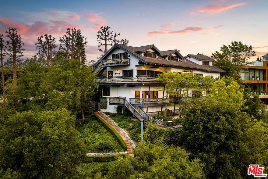 Set on an 18,300 square foot lot between the Riviera and Sullivan Canyon, this 5,345 square foot post-and-beam farmhouse offers privacy, character, and timeless California charm. Tucked behind private gates and surrounded by mature oak trees, the property exudes tranquility with grassy meadows, meandering nature paths, and sweeping canyon views. Inside, five bedrooms and six bathrooms are thoughtfully arranged across a floor plan that blends classic farmhouse design with modern functionality. The gourmet kitchen features a center island and walk-in pantry, flowing into a cozy breakfast nook with a fireplace. Relaxed living areas and the dining room are framed by multiple sets of French doors that open to verandas and patios, creating a seamless indoor-outdoor connection. The primary suite spans an entire level and includes a spacious walk-in closet, spa-like bath with dry sauna, study, and private balcony. Additional highlights include a secondary family room with kitchenette, a dedicated laundry room, and a large storage or archive room with separate access. In the backyard, a pool and spa are nestled among oak trees and lush landscaping, while a swing set, sun deck, and multiple lounge areas offer ample space for entertaining or unwinding. Blending natural beauty with thoughtful design, this private retreat embodies the best of California living in one of Los Angeles' most coveted neighborhoods.