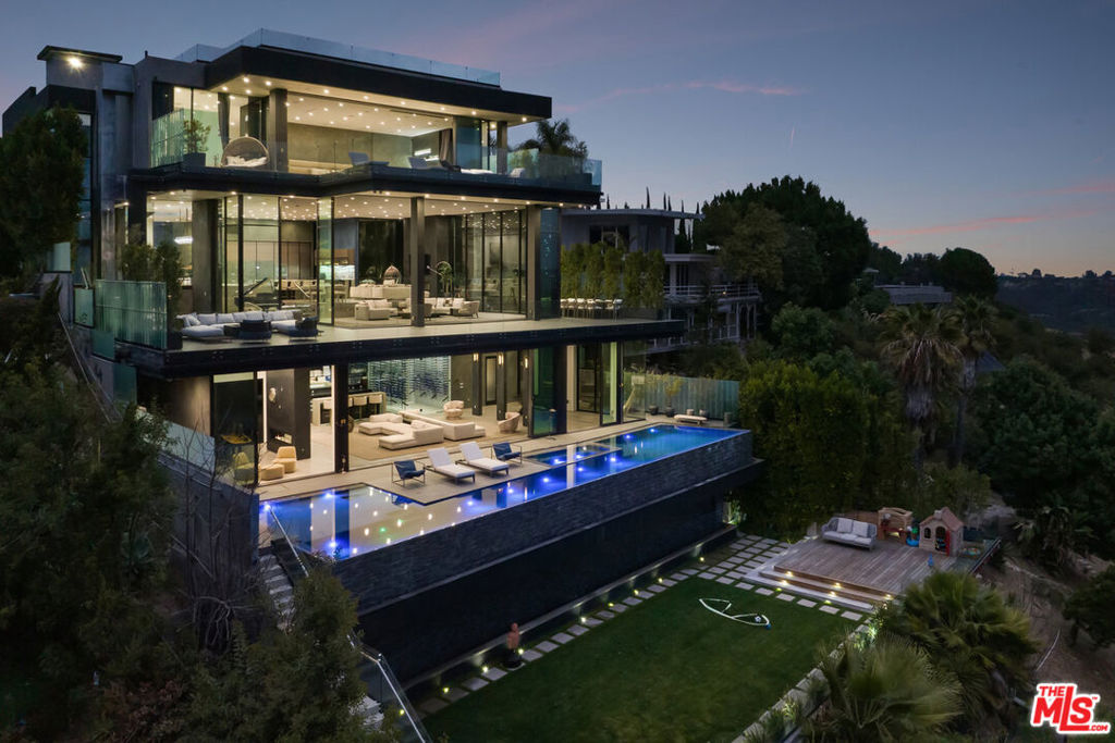 Nestled in prestigious Bel Air, this architectural masterpiece redefines modern luxury with impeccable design and breathtaking views of the hills and lake. The custom Italian-designed kitchen boasts sleek black countertops, a waterfall island, and a striking glass-enclosed wine cellar. The decadent primary bath is adorned with exotic Spanish tiles and features a steam shower, a soaker tub, dual stone sinks, and a double-sided fireplace. Spanning four levels accessible by a private elevator, this home offers an oversized entertainment space, a 1,000+ bottle walk-in wine cellar, a gym, and more. Additional amenities include a gated driveway, a 5-car garage, a Sonos sound system, LED lighting, crystal chandeliers, and exquisite white oak floors. Seamless indoor-outdoor flow is enhanced by floor-to-ceiling glass walls, leading to expansive terraces and an infinity-edge pool that blends harmoniously with the serene surroundings. This Bel Air estate is a showcase of elegance, sophistication, and ultimate comfort.