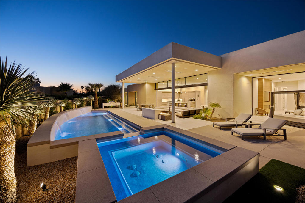Welcome to this cutting-edge desert contemporary masterpiece, a fully furnished 4-bedroom, 6-bathroom estate offering 5,048 sq ft of refined luxury and sophisticated design. Situated on a premium cul-de-sac lot with highly sought-after southwest exposure, this residence captures breathtaking, panoramic mountain range views and delivers resort-style living at its finest.From the moment you enter through the dramatic pivot front door, you're greeted by 14-foot ceilings, a custom 9-foot fireplace, and motorized pocket sliding doors that seamlessly blend indoor and outdoor living in the expansive great room. A step-down bar and a stunning glass-enclosed wine room add flair to your entertaining space, while the adjoining dining area features manual pocket sliders for effortless flow.The chef's kitchen is outfitted with top-of-the-line Wolf and Sub-Zero appliances, a substantial walk-in pantry with built-in cabinetry, a full-size refrigerator, and an integrated coffee station--perfect for hosting or daily luxury.Each of the four en-suite bedrooms, including a private office, features direct access to the exterior, offering serene transitions to the landscaped surroundings. The primary suite is a true retreat with a spa-like bath, dual water closets, and sliding doors that lead to a secluded outdoor tranquility garden.Outdoors, the resort-style amenities continue with a custom pool and spa, a full outdoor entertainment center with pop-up TV, fire ledge, recessed electric heaters, and a mist system for year-round comfort. A covered structural patio overhang and 36x36 tile flooring that flows from the interior to the exterior enhance the seamless, modern design.Additional features include a private, gated, motor courtyard, four-car garage (~1,165 sq ft) with two AC units, Sonos sound system throughout the home including interior and exterior and custom lighting and premium finishes throughoutThis home redefines high-end desert living--resort never looked so good.