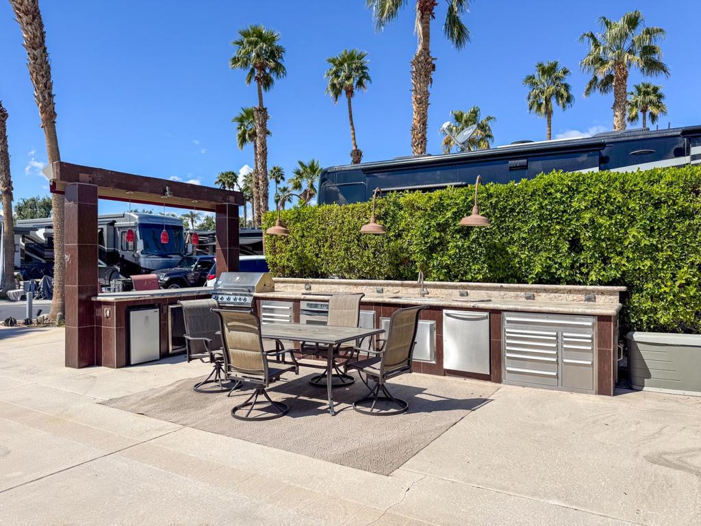 This private, perimeter luxury RV lot is an entertainer's paradise, boasting a spacious gourmet kitchen with a beautiful arch-front bar and retractable awnings for shade and comfort, all perfectly positioned to capture breathtaking sunset views. Outfitted with stainless steel appliances, granite countertops, and a large sink with hot water, the kitchen includes a built-in oven, cooktop, BBQ, fridge, dishwasher, and ample storage, ensuring effortless meal preparation and hosting. Mid-lot hookups provide convenience, while the furnished space creates an inviting atmosphere for relaxation and entertainment. Outdoor Resort Indio is a class A only motorcoach resort.
