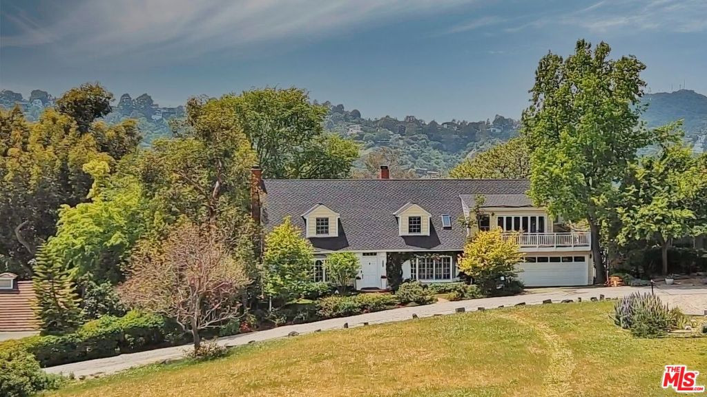 Up a private drive, this warm & inviting classic two story home resides on a generous flat parcel in an exclusive park-like setting above the lovely Lake Hollywood Reservoir. Cherished for 40 years by the same meticulous owners who have thoroughly enjoyed its dazzling views, uncommon privacy & super convenient location, this light-bathed home exudes a tranquil ambiance that feels as if you may have been transported to Provence. From the primary suite balcony at dawn, most days begin with vibrant sunrises that break over the hills of Griffith Park to the downtown skyline before lighting up the the iconic Hollywood Sign, the Griffith Park Observatory & the occasional family of deer grazing on the pasture that stretches 100 feet in front of the house. In early evenings on the charming brick patio surrounding the sun-drenched pool, most days end with brilliant sunsets that melt behind the silhouette of the Hollywood Hills. During the day, lush landscaping & mature trees that flank the patio pool deck offer several spaces for moments of contemplation, inspiration & relaxation - reminiscent of a private romantic villa tucked away in the foothills of northern Italy or southern France. Inside, original hardwood floors, crown moldings and French doors/windows provide a comforting sensibility throughout a floor plan that includes a grand living room with fireplace, a formal dining room adjacent to a cheerful white tiled eat-in kitchen & a den/4th bedroom with fireplace downstairs - all with French doors that invite in the light and the fresh afternoon breeze. Up a formal staircase the second level features a generous 2nd bedroom with built-ins, a large vintage tiled bathroom, a 3rd en suite bedroom with balcony and a sumptuous primary suite with a high pitched ceiling, spa like bathroom that feels like a treehouse, walk-in closet, fireplace and that spacious balcony overlooking those superb views. With a home life so serene in this extraordinary setting near acres of open space & miles of hiking trails, you'll have a hard time believing that most major studios, downtown & Hollywood are all just minutes away. It just might take you 40 years to believe you've found this slice of heaven in the heart of Los Angeles.