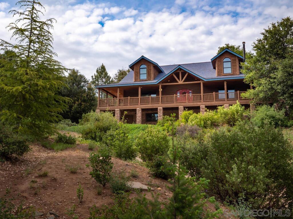 Welcome to Mountain Majesty, a luxurious log home nestled in the private, gated community of Julian Estates. Built in 2007 and thoughtfully enhanced by its current owners, this custom-crafted retreat offers timeless mountain charm, elegant craftsmanship, and quality finishes throughout. Set on a gently sloping, tree-lined lot, the home is surrounded by natural beauty and privacy. A spacious wrap-around deck welcomes you outdoors to enjoy fresh mountain air, forest views, and year-round entertaining. Custom stone veneer detailing surrounds the lower entry, pillars, stairwell, built-in BBQ area, and lower patio, adding texture and character to every corner. Inside, the home features 3 bedrooms, 3.5 bathrooms, a cozy loft, and a bonus room that’s ideal as a media room, game room, studio, or guest suite. The interior showcases vaulted wood ceilings, richly grained paneling, and finely crafted woodwork throughout. "Continue in Supplement" The heart of the home is the open-concept kitchen, beautifully appointed with granite countertops, custom cabinetry, and a sleek mosaic tile backsplash that adds a modern touch. This kitchen seamlessly connects to the living and dining areas, perfect for casual meals or formal entertaining. The primary suite offers generous proportions, forest-facing windows, and a tranquil ensuite bathroom that features a travertine walk-in shower, a classic clawfoot tub, and thoughtful finishes that combine rustic style with refined comfort. A true highlight is the private spa and sauna room, designed for rejuvenation and relaxation. A wall of windows floods the space with natural light, creating a serene retreat with views of the surrounding woods. Outdoors, enjoy a fully enclosed gated fruit and vegetable garden, perfect for seasonal harvests and hobby gardening. The property also includes a 19'x24' 2-car garage, a dedicated 14'x49' workshop, and abundant storage space to accommodate tools, equipment, and outdoor gear. Essential infrastructure includes a whole-house Generac generator, tankless water heater, ductless mini-split HVAC systems, water softener, custom-encased irrigation valve control stations, strategically positioned for optimal water distribution and streamlined system management, a detached pump house with a 10,000-gallon water storage tank and a wharf hydrant, ensuring comfort, efficiency, and peace of mind. Located in one of Julian’s most desirable neighborhoods, this exceptional property offers the best of mountain living with privacy, security, and luxury all in one. Whether you’re looking for a full-time home, a high-end second residence, or a turnkey mountain getaway, Mountain Majesty delivers quality, character, and timeless appeal. "Come and experience a lifestyle worth living in a community where we call home."