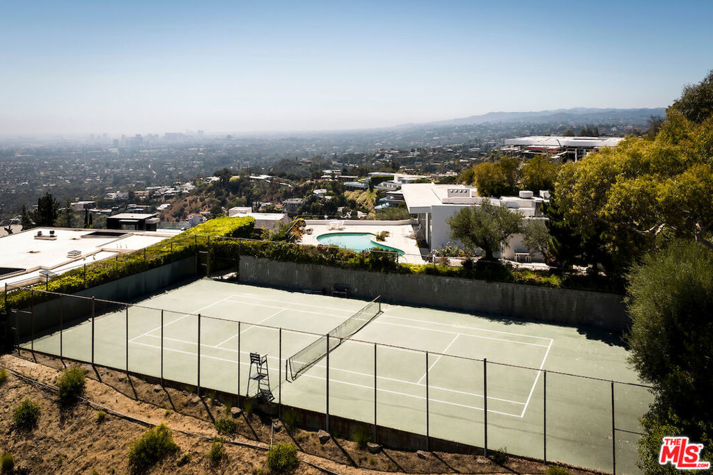 First time this extraordinary tennis court estate in the Bird Streets has been on the market in 50 plus years. Situated at the top of one of the most exclusive streets in the Hills, this double lot, totaling 32,564 square feet, showcases unobstructed views from Downtown Los Angeles to the Pacific Ocean. Experience the ultimate tennis match on the full size court, on a completely flat pad, with a backdrop of breathtaking views and a second driveway for direct access. Spanning just over 3,000 square feet, this 3 bedroom, 3 bathroom, mid century residence has been exceptionally maintained. A functional open concept floor plan welcomes guests into the living room with a built in bar and wall-to-wall glass sliding doors which welcome in an abundance of sunlight and lead out to the expansive patio with an in-ground pool. The dining room seamlessly incorporates a central atrium with a tranquil fountain amongst lush foliage. The primary retreat features generous closet space and a swanky en suite. Revel in this truly rare opportunity to acquire one of the few tennis court estates in the Bird Streets.