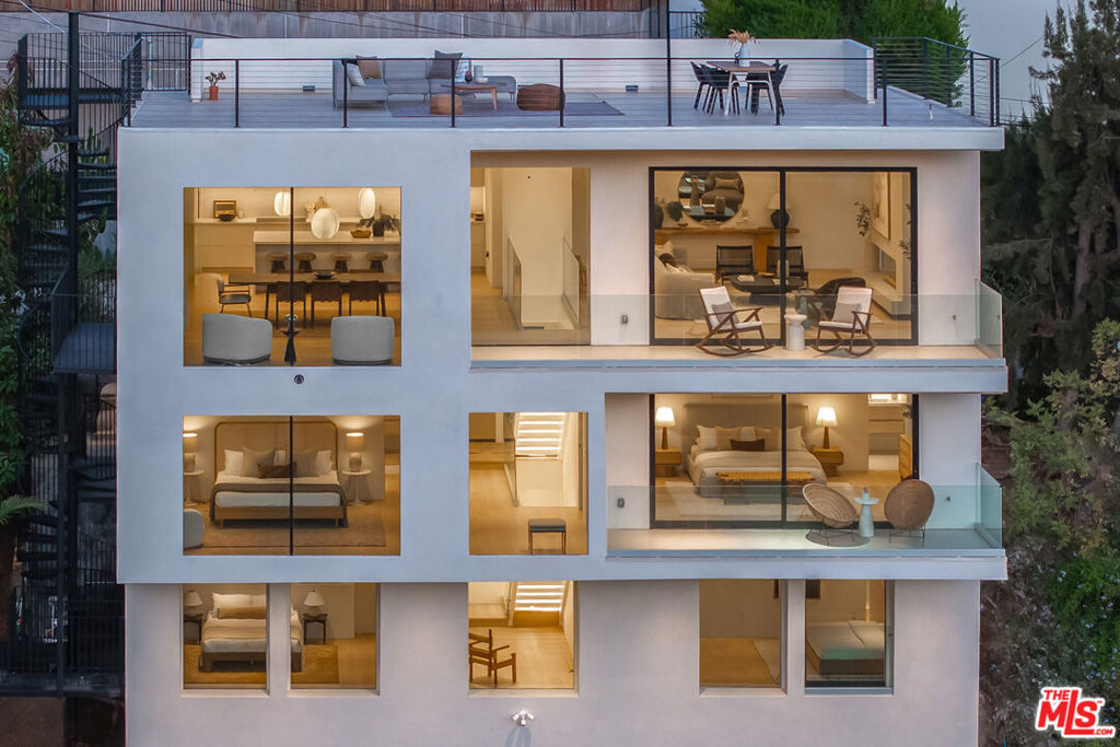 Perched above the coveted enclave of Rising Glen, this completely renovated custom residence offers sophisticated modern living with sweeping 180-degree hillside views. Thoughtfully designed with clean lines, tone-on-tone finishes, and an emphasis on natural light, the home features four bedrooms and three and a half bathrooms within a seamless open-concept layout. Connecting the levels with quiet elegance, the softly lit floating staircase sets a graceful tone. The upper level offers a generously sized main living area anchored by a custom-designed fireplace with a subtly textured plaster finish. Pale wood-toned flooring, floor-to-ceiling glass, soaring ceilings, bespoke lighting, and soft natural light contribute to a calm, airy atmosphere. The chef's kitchen balances form and function with a complete suite of integrated Miele appliances, custom cabinetry, a waterfall-edge island, a dry bar, and a ZipWater HydroTap. Expansive glass-railed terraces extend the living space outdoors, ideal for morning coffee or relaxed sunset gatherings. Each of the four bedrooms provides a peaceful retreat with treetop views and spa-inspired bathrooms. The top level includes the potential for a private rooftop deck with panoramic hillside, city, and peekaboo ocean views. In the backyard, a detached structure adds versatility, and could serve as a creative studio or wellness space. Located minutes from the Sunset Strip yet tucked away in a quiet elevated setting, this home blends modern elegance, thoughtful design, and privacy in one of Los Angeles' most desirable neighborhoods.
