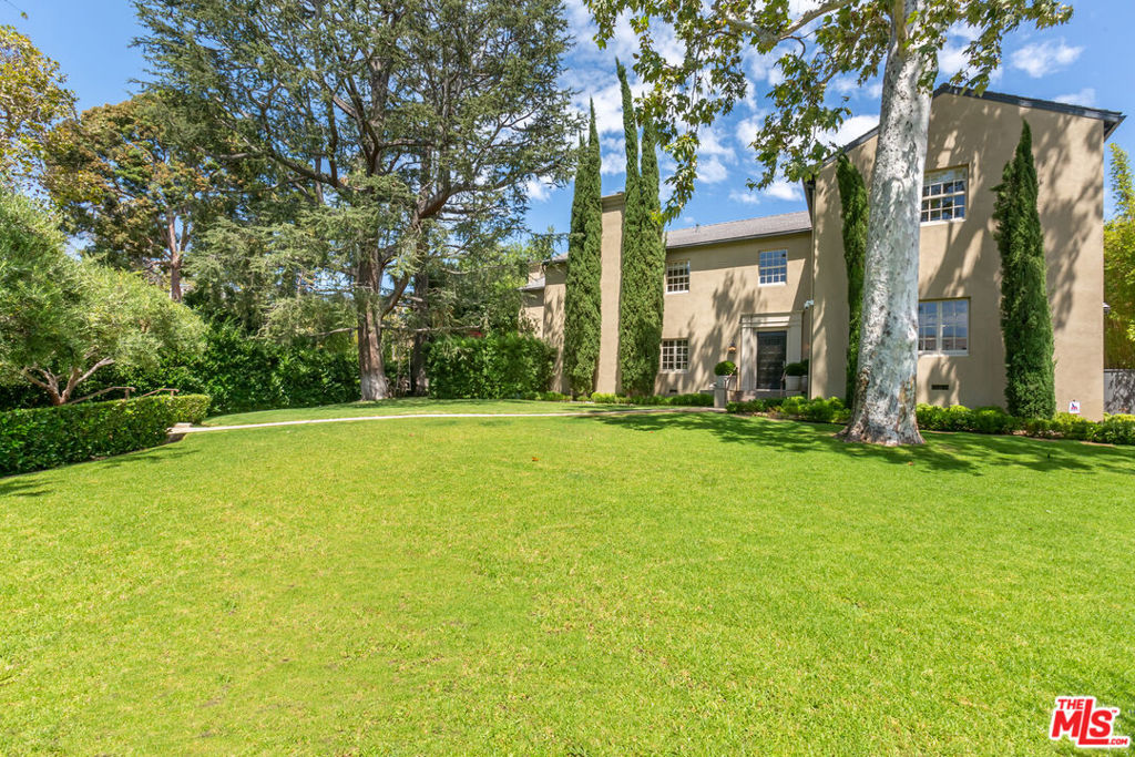 Situated on a sprawling and lush property, the Hudson Estate is a sanctuary on one of the premier corners of Hancock Park. Surrounded by mature landscaping, the home boosts exceptional privacy - an extremely rare and coveted attribute for the neighborhood. The main house features six generously sized bedrooms, including a luxurious primary suite with dual bathrooms, walk-in closets, and a private office overlooking the expansive grounds. A formal living room with coffered ceilings and fireplace opens to a bright patio, creating an effortless indoor-outdoor flow ideal for entertaining. The chef's kitchen includes high-end appliances and abundant counter space, connecting to a cozy family room with its own fireplace, projector, and hidden movie screen. A paneled formal dining room offers garden views, while additional spaces including a separate office and gym enhance the estate's versatility and comfort. Each of the five guest bedrooms upstairs includes en-suite baths, ample closets, and natural light. In addition to the main residence, a detached guest house provides flexible space for extended family, visitors, or creative use. The meticulously landscaped grounds are anchored by a resort-style pool and multiple outdoor living areas, perfect for entertaining or quiet enjoyment. This exceptional property is a rare offering in one of Los Angeles's most sought-after neighborhoods.