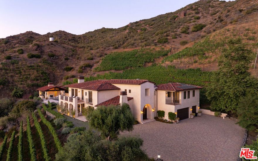Nestled in the rolling hills of Malibu wine country, 33330 Hassted Drive is a one-of-a-kind vineyard estate where refined living meets natural beauty. Set on a hillside surrounded by mature vines and breathtaking mountain views, this gated retreat offers complete privacy and timeless Mediterranean charm.The main residence is thoughtfully designed with warm stucco exteriors, red-tile roofing, and hand-finished details that echo the rustic elegance of the European countryside. Inside, soaring ceilings, arched hallways, and carved stone fireplaces create a sense of understated luxury. Expansive windows and French doors flood the home with light and frame sweeping vistas of the Santa Monica Mountains from nearly every room.The chef's kitchen is both beautiful and functional, featuring dual center islands, premium appliances, and an open layout ideal for entertaining. Living areas flow effortlessly outdoors to a spectacular pool terrace lined with lounge seating and anchored by a resort-style cabana. Complete with its own fireplace, bar, and shaded dining space, the cabana is designed for unforgettable gatherings from day to night.As the sun sets, the estate transforms into a private cinematic experience with a custom, oversized outdoor movie screen that rises seamlessly from the groundoffering open-air screenings under the stars with the surrounding vineyard as your backdrop. For a more immersive experience, the home also features a dedicated indoor theater room, creating a true dual-screen lifestyle for both indoor comfort and outdoor drama.The primary suite offers a peaceful sanctuary with a private balcony, cozy fireplace, and spa-like bath. A freestanding clawfoot tub is perfectly positioned to take in the surrounding ridgelines, while dual vanities and a large walk-in dressing room with custom cabinetry provide elevated functionality and style.Additional spaces include a handsome wood-paneled office with built-in library shelving and French doors leading to a private patio. A detached guest house offers beautiful accommodations for visitors or staff, while a spacious motor court and three-car garage provide ample parking. Modern comforts are integrated throughout, including a solar panel system and smart home features.From its walkable vineyard rows and inviting interiors to its resort-style amenities and rare cinematic touches, 33330 Hassted Drive is a fully realized Malibu retreat designed for inspired living and unforgettable entertaining.