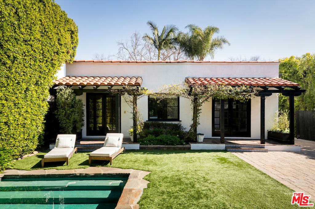 Serene, private West Hollywood bungalow. Concealed behind mature hedges and gates is this turn-key, two bed, two bath idyllic retreat. Spanish tiles and a rose garden lead guests past a charming, vine adorned patio, with a fountain, into the arched main entrance. A cozy stone fireplace is the focal point of the formal living room that is met with soaring, curved ceilings and oversized picture windows that invite in an abundance of natural sunlight. Dark wood trim around the dining room perimeter perfectly compliments the cabinetry and marble countertops in the chef's kitchen that is fully equipped with stainless steel appliances and a generous center island. Tucked away on its' own wing, the primary suite offers custom built-in's, French doors to the backyard, and a luxurious en-suite with dual sinks, a soaker tub and a stand alone shower. This sprawling lot, reminiscent of a tropical oasis, is an entertainer's dream. A sparkling pool, situated adjacent to the abundant grassy pad, nestles up to a fire pit and outdoor dining area for harmonious indoor-outdoor living. Blossoming floral and citrus trees further enhance this tranquil haven. Top of the line outdoor lighting illuminates the nightscape for evening enjoyment. French doors seamlessly convert the two car garage into a pool house. Experience trendy dining, shops, and entertainment just moments away on the iconic Melrose Ave.