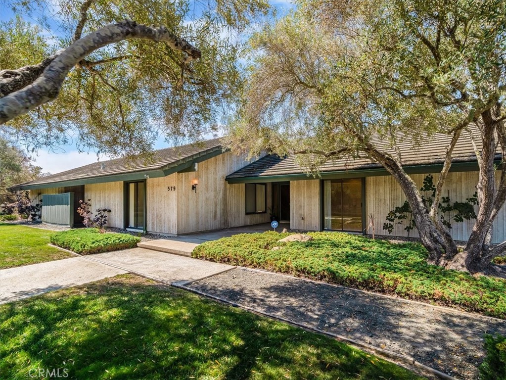 Tucked deep within the desirable Lompoc Country Club neighborhood this expansive 0.59 acre lot is perched atop a quiet ridge with commanding vistas. With 3 bedrooms and 3 bathrooms, this generous 2,432 square-foot residence is a timeless blend of classic architecture and breathtaking natural surroundings. Step inside to find sun-drenched interiors, an inviting open floor plan, and spaces that strike a perfect balance between lively entertaining and quiet retreat. The living room features a dramatic fireplace focal point and expansive views of the gardens and golf course. Glass doors open to a series of patios and outdoor vignettes, ideal for morning coffee or evening gatherings. The spacious, light-filled kitchen is outfitted with custom cabinetry, a built-in bar and breakfast area, and direct access to both the formal dining room and a covered patio — making indoor/outdoor living effortless. The primary suite is a tranquil retreat, offering sweeping views, abundant natural light, and a deep sense of privacy. The en-suite bathroom with dedicated vanity area and walk-in closet complete this luxurious oasis. The second bedroom offers flexibility to restore its original configuration as two separate rooms — perfect for a guest suite, home office, or den. The third bedroom is privately situated in its own wing of the home, with front garden views. A two car garage includes a fully finished workshop or office, along with ample built-in cabinetry for storage and organization. Outside, the landscaped grounds are a natural extension of the warm and intentional design, featuring covered patios, an heirloom rose garden, native plants, mature trees, and breathtaking golf course vistas.