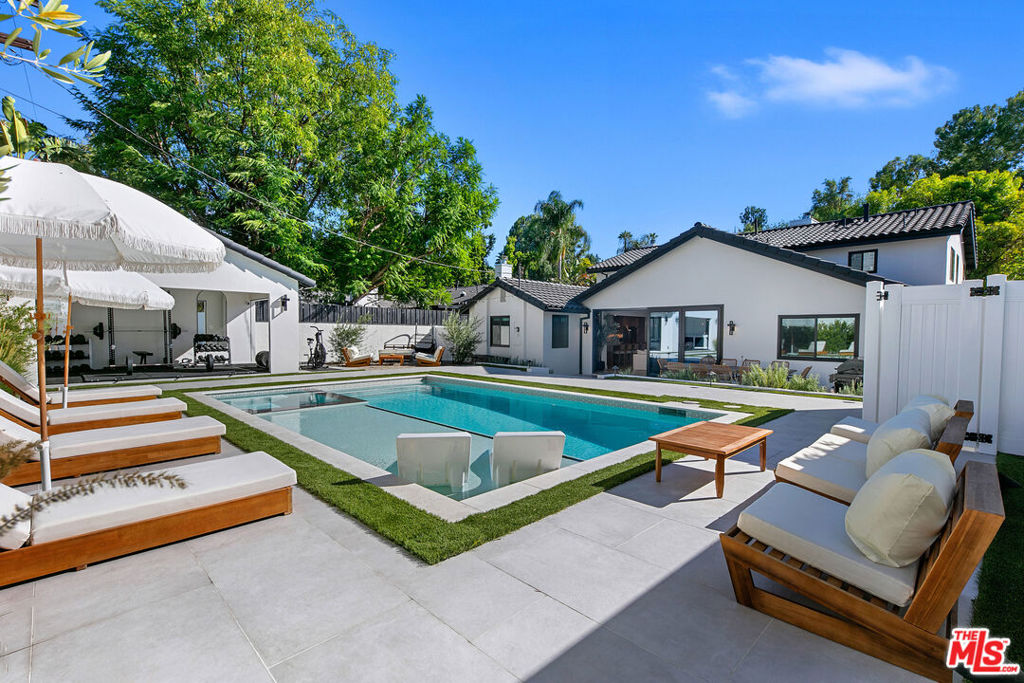 Contemporary Woodland Hills retreat with a resort-style pool and cabana! Tucked behind gates on a beautifully landscaped lot, this extensively renovated custom home blends upscale design with the ease of indoor-outdoor California living. Designed with high-end finishes throughout, including Roman Clay walls, soaring ceilings, and wide-plank White Oak floors, the home exudes a warm yet sophisticated aesthetic. The main level features a light-filled living room with a gas fireplace and an elegant dining area with a built-in bar. The gourmet kitchen is a chef's dream, complete with Thermador appliances, a walk-in pantry, and a center island with bar seating. Adjacent to the kitchen, there's a versatile media room, and an open-concept family room with a gas fireplace that flows seamlessly through sliding accordion doors to the backyard oasis. Outside, you'll find a sparkling pool and spa, al fresco dining, multiple lounge areas, and a cabana currently set up as a gym yet easily adaptable for an entertaining space. Upstairs, the luxurious primary suite boasts a gas fireplace, dual walk-in closets, a built-in vanity, and a private balcony. The spa-inspired bathroom offers a freestanding tub and refined finishes. All bedrooms are en-suite, with two conveniently located on the main level and the remainder upstairs, ensuring privacy and comfort for family and guests. Additional highlights include a temperature-controlled wine cellar, ample storage, a two-car garage, and a drive-in/drive-out motor court. Conveniently located near the 101 and moments from local amenities such as The Commons at Calabasas, The Village, Westfield Topanga, markets, and dining, this residence embodies upscale Woodland Hills living at its finest.