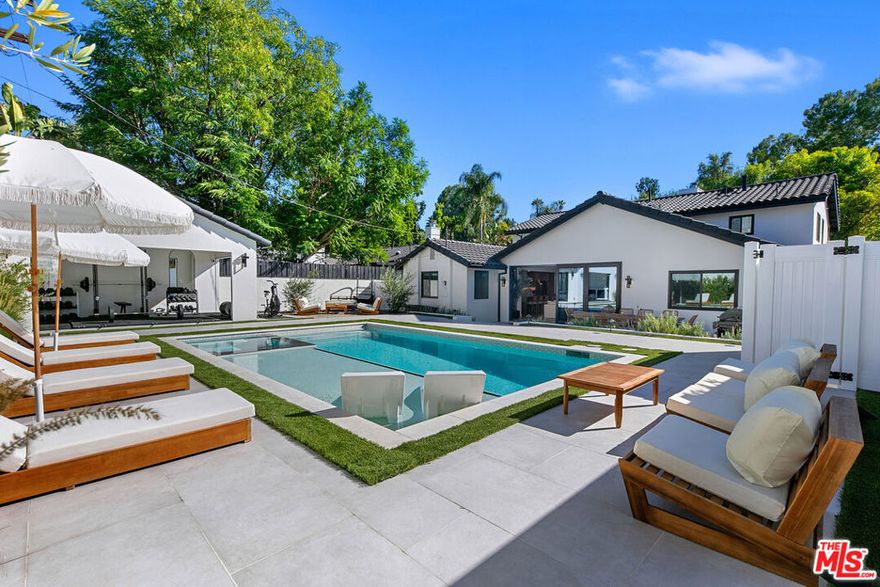 Contemporary Woodland Hills retreat with a resort-style pool and cabana! Tucked behind gates on a beautifully landscaped lot, this extensively renovated custom home blends upscale design with the ease of indoor-outdoor California living. Designed with high-end finishes throughout, including Roman Clay walls, soaring ceilings, and wide-plank White Oak floors, the home exudes a warm yet sophisticated aesthetic. The main level features a light-filled living room with a gas fireplace and an elegant dining area with a built-in bar. The gourmet kitchen is a chef's dream, complete with Thermador appliances, a walk-in pantry, and a center island with bar seating. Adjacent to the kitchen, there's a versatile media room, and an open-concept family room with a gas fireplace that flows seamlessly through sliding accordion doors to the backyard oasis. Outside, you'll find a sparkling pool and spa, al fresco dining, multiple lounge areas, and a cabana currently set up as a gym yet easily adaptable for an entertaining space. Upstairs, the luxurious primary suite boasts a gas fireplace, dual walk-in closets, a built-in vanity, and a private balcony. The spa-inspired bathroom offers a freestanding tub and refined finishes. All bedrooms are en-suite, with two conveniently located on the main level and the remainder upstairs, ensuring privacy and comfort for family and guests. Additional highlights include a temperature-controlled wine cellar, ample storage, a two-car garage, and a drive-in/drive-out motor court. Conveniently located near the 101 and moments from local amenities such as The Commons at Calabasas, The Village, Westfield Topanga, markets, and dining, this residence embodies upscale Woodland Hills living at its finest.