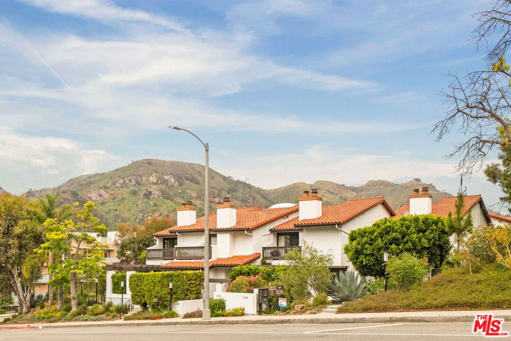 On the quiet curve of Palisades Drive, this expansive townhome unfolds with over 2,000-square-feet of natural light, volume, and functional design in the Palisades Highlands. A gated front entry leads to a dramatic interior where soaring beamed ceilings crown the main living room, anchored by a wood-burning fireplace and framed by sliding doors that open to a fenced terracotta patio ideal for al fresco dining or quiet evenings under the stars. The living room flows effortlessly up to a formal dining area and built-in bar with an elevated vantage point ideal for entertaining. The adjoining kitchen features stainless steel appliances including double wall ovens, a reverse osmosis water system, and a dedicated breakfast nook illuminated by soft morning light. Around the corner, a powder room completes the main level. Upstairs, the expansive primary suite is a true retreat, with vaulted ceilings, two generous walk-in closets, a spacious en-suite bath with dual vanities, and sliding glass doors that lead to a private balcony with mountain vistas. The upper level continues with two guest rooms and a second full bath, offering flexibility for guests, an office, and more. Additional highlights include an attached two-car garage with direct access, ample storage, and in-unit laundry. Recent upgrades include the HVAC system, dishwasher, and washer/dryer -- all completed in 2018. Residents enjoy exclusive access to a beautifully updated gym with a sauna, pool, and spa, surrounded by lush grounds and canopied hillsides. Set just moments from beloved local hiking trails and a quick drive from Palisades Village, 1559 Palisades Drive offers the ideal opportunity to live in one of the most sought-after enclaves on the Westside.