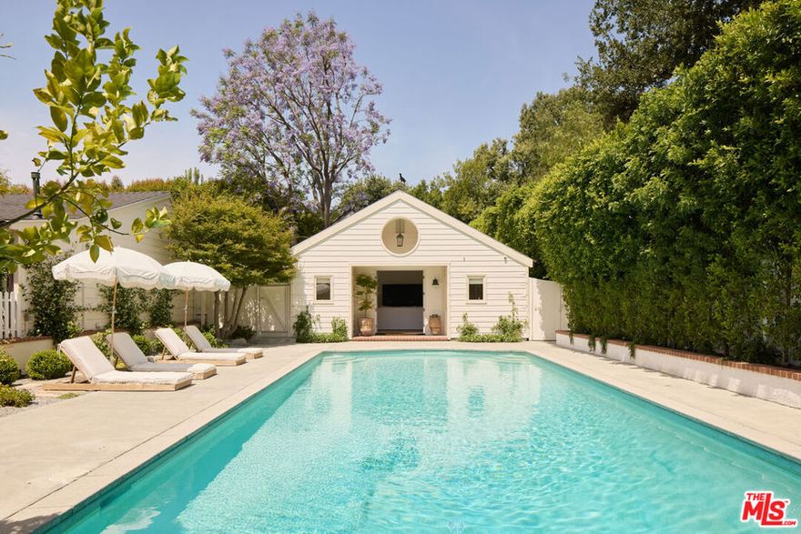 Tucked discreetly behind a wrought-iron gate and up a long, picturesque driveway that crosses a charming bridge, this beautifully reimagined ranch-style retreat offers a rare blend of privacy and allure. Sheltered beneath a canopy of oak trees and framed by vibrant rose gardens, the home exudes warmth and sophistication. Meticulously remodeled with high-end finishes and an exceptional eye for detail by interior designer Paula Bruss, the single-story residence is filled with natural light, thanks to expansive windows that capture the sun from dawn to dusk. Vaulted ceilings, refined stone and tile work, designer fixtures, and architectural character elevate every room with timeless charm. French doors open to an enchanting backyard oasis, with a spectacularly oversized swimming pool and lush green lawn perfect for relaxing, entertaining, or simply enjoying the serenity of nature. The long paver-stone driveway leads to a spacious motor court with ample parking, in addition to a two-car attached garage. A separate, private guest house complete with a full bathroom and kitchenette offers ideal accommodations for guests, extended family, or a home office. The main residence includes three bedrooms (one of which is currently converted into a custom closet but can be easily reverted), spanning approximately 3,770 sq ft. The guest house adds an additional approximate 400 sq ft of well-appointed living space.