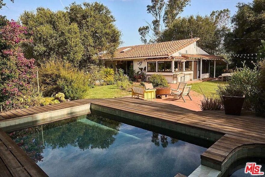 The School Road Ranch is not just a home-it's a living, breathing experience of Topanga Canyon life at its most soulful. Perched gracefully on a gentle knoll in the heart of the Canyon, this 1.85 acre sprawling compound offers a rare blend of privacy, creativity, and connection to nature. Here, warm southern light filters through ancient oaks, cool ocean breezes drift up from the Pacific, and expansive canyon views unfold in every direction. The property spans nearly 2 acres of vibrant, usable land, a sanctuary where families, artists, and seekers of beauty can truly thrive. From the moment you step through the rustic wooden gate, the outside world dissolves. You're greeted by rolling green lawns, flowering native gardens alive with hummingbirds, and winding pathways that lead to secret spaces: a hidden bamboo forest, decks suspended in the view, and sun-drenched spots perfect for reflection or shared meals under the sky. This is a place where children can run barefoot, where creativity has room to breathe, and where life slows down to meet the rhythms of nature. The main house has been reimagined with reverence for craftsmanship and texture, honoring both the land and a lineage of soulful design,  creating a space of peace and tranquility. Reclaimed wood ceilings, handmade Indonesian carved doors, and artisan windows frame the changing light throughout the day. The great room welcomes you with soaring open-beamed ceilings, a glowing fireplace, and wide plank oak floors that invite bare feet and long, quiet mornings. The kitchen is both functional and inspirational outfitted with True, Viking, and Sub-Zero appliances offering space to create nourishing meals with family and friends. The primary suite is more than a bedroom; it's a retreat for the spirit, designed as an open-concept sanctuary where rest, reflection, and renewal happen naturally. Soak in the deep copper tub while gazing at distant mountain views, step onto the private sun deck after a restorative bath, or slide the handcrafted wall to create quiet separation when needed. Two additional bedrooms and a thoughtfully designed bath complete the main home, offering comfort and flow for loved ones. Scattered across the property are spaces designed for creativity, connection, and quiet solitude. Two fully self-contained guest units each with private entrances, kitchenettes, and baths are perfect for visiting family, creative residencies, or generating rental income while maintaining privacy. One guest house features a separate sleeping area with warm hardwood floors and custom finishes; the other offers an open studio layout ideal for writing, painting, or quiet retreat. An additional office cabin, potting shed, and secret gardens woven throughout the landscape provide endless opportunities for discovery and reflection. The grounds have inspired countless fashion and product shoots, but the true beauty is how naturally life unfolds here: dinners under the stars, early morning swims, trails that lead to new ideas, and spaces that hold both community and solitude in balance. 22068 Topanga School Road is a property for those who value intention, beauty, and belonging. It's for those who want to grow together in nature, for artists seeking inspiration, and for travelers ready to root themselves in a place where creativity, consciousness, and connection to the earth are part of daily life. This is the Topanga Life fully realized.