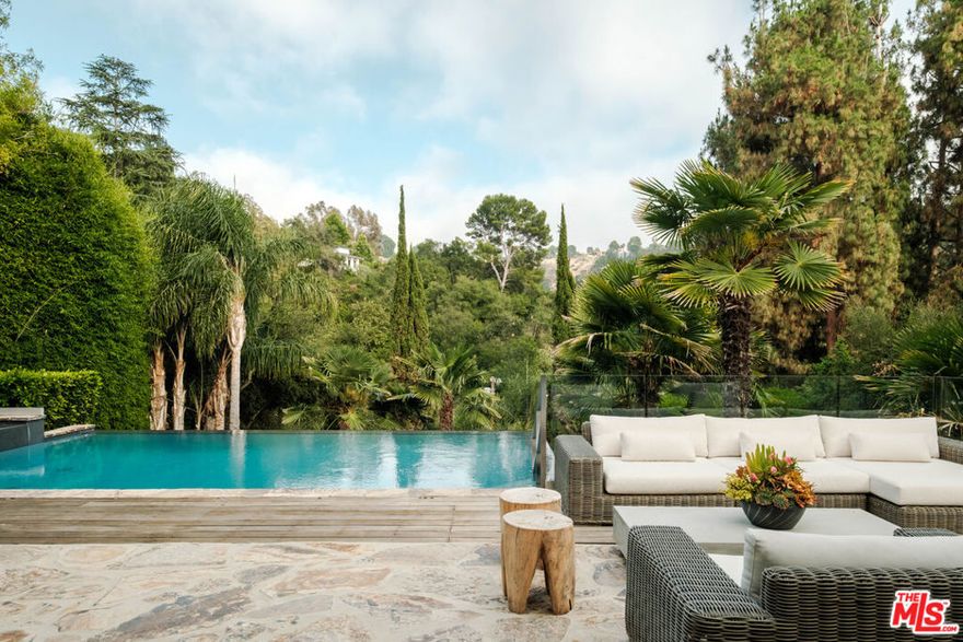 Where architecture meets altitude, this gated Beverly Hills estate is a sanctuary of modern luxury and timeless sophistication. This former celebrity residence is nestled above the street in the prestigious Old Hutton Drive enclave of Benedict Canyon. Spanning nearly half an acre, the contemporary estate commands breathtaking canyon views while offering rare privacy and serenity. Designed for those who value both beauty and function, the home transitions effortlessly from moments of quiet retreat to unforgettable gatherings in grand style. The living room, crowned with soaring 14-foot ceilings, opens through expansive sliding glass doors to an entertainer's terrace with a spa, cabana, and infinity-edge pool cascading into the canyon, creating a showstopping backdrop by day or night. Just off the chef's kitchen, the family room flows to a grass backyard with alfresco dining and lush landscaping, offering multiple destinations to host, relax, and celebrate. Inside, natural light floods the interiors, illuminating a refined palette of stone, wood, and glass that harmonize with effortless elegance. Each bedroom is ensuite, highlighted by a full-floor primary retreat with a spa-like bath, boutique-style closet, and two private decks with sweeping canyon vistas. A secondary main-level primary suite and oversized guest rooms provide flexibility and comfort. Additional highlights include a gym, den, ample parking for numerous vehicles, and potential space for a sports court or ADU. This estate embodies the essence of Beverly Hills living -- exclusive, inspiring, and built to entertain on any scale.