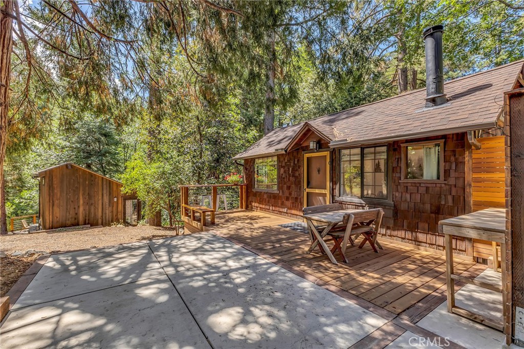 Nestled among towering pines, this enchanting 1934 cabin offers timeless character, thoughtful updates, and a setting that feels soul-soothing from the moment you arrive. The property pairs vintage charm with modern convenience, creating a retreat that is as inspiring as it is peaceful. Inside the main cabin, the warmth of wood-beamed ceilings and original wood floors speaks to the history of the home, carrying with it nearly a century of mountain living. A rock hearth with wood stove brings rustic authenticity, while upgraded windows frame views of the lush forest and fill the interior with natural light. Subtle improvements, including a newer roof and updated electrical, provide peace of mind without compromising the cabin’s charm. Step outside and discover a newly built deck that flows onto a spacious patio, perfect for quiet mornings with coffee, summer gatherings, or evenings under the stars. The outdoor spaces are designed to enhance the experience of living in nature while still being in town. Wild berries line the drive each spring and summer, a reminder of the property’s natural abundance. From the edge of the lot, a sweet meandering path winds toward town, offering a shaded walk beneath the trees. The detached studio, added in 2023, provides an entirely different experience. With soaring ceilings, its own deck, a sleeping or storage loft, and walls of glass overlooking the trees and a seasonal creek, it is a space that feels both modern and magical. Perfect for use as a guest suite, office, yoga or art studio, or simply a quiet place for reflection, the studio expands the property’s versatility while blending seamlessly with its natural surroundings. Additional features include ample parking, a newly built deck, and an EV charging station for added convenience. Though the property is only moments from restaurants, shops, and community life, it feels worlds away, offering the hush of nature and a true sense of solitude. This is more than a home. It is an Idyllwild escape where vintage charm, modern comfort, and the quiet beauty of the forest come together in perfect harmony.