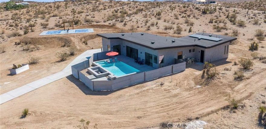 Luxury Desert Retreat with Pickleball Court, Pool & Spa, and Sunken Fire Pit: 3 Bedrooms 2 Bathrooms 2 Car Garage Fully Furnished.



Experience the ultimate desert lifestyle in this brand-new modern home, perfectly designed for both relaxation and entertainment. Located in the highly sought-after Joshua Tree area, this property immediately impresses with its resort-style outdoor amenities—a private pickleball court, sparkling in-ground pool and spa, and an expansive sunken fire pit, all set against breathtaking desert and mountain views.



Set on 2.09 private acres with convenient paved-road access via a concrete driveway, this custom-built residence combines contemporary architecture with desert serenity. The home was masterfully crafted by renowned local builder Darrell Danielson, who brings over 40 years of expertise to every detail.



The striking butterfly roofline and walls of glass frame panoramic views of Pipe Canyon and the San Gorgonio Mountains. Inside, the open-concept great room features soaring ceilings, polished concrete floors, and a sleek linear electric fireplace. Oversized sliding glass doors connect indoor living with the dramatic outdoor landscape, creating seamless flow throughout.



The chef’s kitchen is both functional and stylish, showcasing a quartz waterfall island, custom European-style cabinetry, premium appliances, and a wine fridge—ideal for entertaining or enjoying everyday meals in style.



Retreat to the spa-inspired bathroom, designed with a soaking tub, walk-in shower, and rain showerhead for ultimate relaxation. Elevated finishes continue throughout with 8-foot doors, an oversized slider, and an insulated 8’ garage door. Energy efficiency is built into the home with high-efficiency AC and appliances, ensuring modern comfort in every season.



Every feature of this property was thoughtfully chosen to enhance the desert lifestyle. Whether you’re enjoying a quiet evening by the fire pit, a friendly pickleball match, or a sunset swim, this home offers an unparalleled retreat. Perfect as a full-time residence, weekend getaway, or high-demand vacation rental, this is truly a one-of-a-kind opportunity to own modern luxury in Joshua Tree.