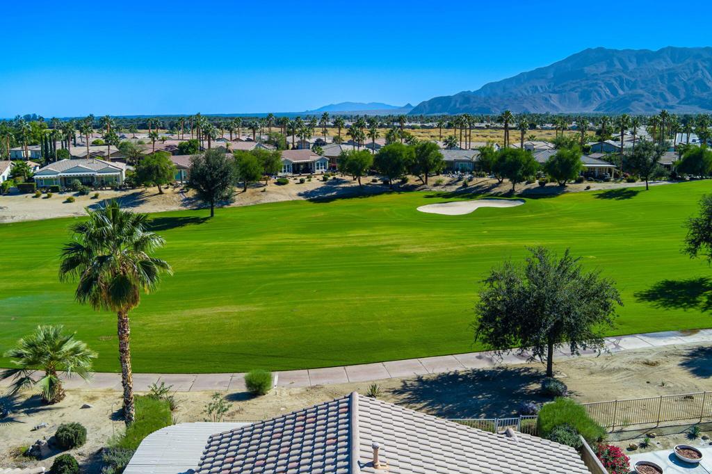 Sunshine, Fairways, and Mountain Views. Located in the heart of the Trilogy Golf Club at La Quinta, this delightful desert retreat makes the most of its sunny and expansive east and southwest golf course and mountain views. The open concept, nine-foot ceilings, and big picture windows open to a large back patio, making this 1,745 SQFT home feel much larger. And, with 2-bedrooms, 2-baths, a den/office, and bonus room, the home easily adapts to all your lifestyle needs. Inside, the home is upgraded with attractive and durable wide-plank luxury vinyl floors that blend seamlessly with the custom stone floors in the bedrooms. The primary bedroom is roomy with plantation shutters, and a large walk-in closet. The primary bath features dual vanities with custom antique white cabinets, and a walk-in steam shower, with custom tile surround and bench seat. The kitchen is open to the dining area with windows overlooking the back patio and big golf course views. Beautiful and efficient, the kitchen is well-organized for cooking and entertaining. Abundant quality antique white cabinets and a pantry keep the kitchen tidy. The counters and the center island are crowned with dreamy quartz, and are complemented by a glass subway tiled backsplash. A double oven, gas cooktop, microwave, double-sided refrigerator/freezer, and a dishwasher make quick work of meal prep. On cool winter days, the family room fireplace is the perfect spot to snuggle up with a good book or to binge-watch your favorite TV show. On warm sunny days, the slate colored tile flooring, a pergola and automated sun shades on the patio keep outdoor living comfortable. Anytime is the best time to watch the early sun rise above the horizon, golfers as they try to top their best scores, and the moon as it glides across the mountain peaks. A guest bedroom and a den with a nearby full bath are separated from the primary bedroom. An added bonus is a separate covered patio with etched glass walls, open to the main living area, and with sliding doors that open to a private patio at the side of the home. The garage fits two cars side-by-side with room for storage, and is air conditioned. Priced to sell this home will not last long. If looking for a golf course property, come see it today!