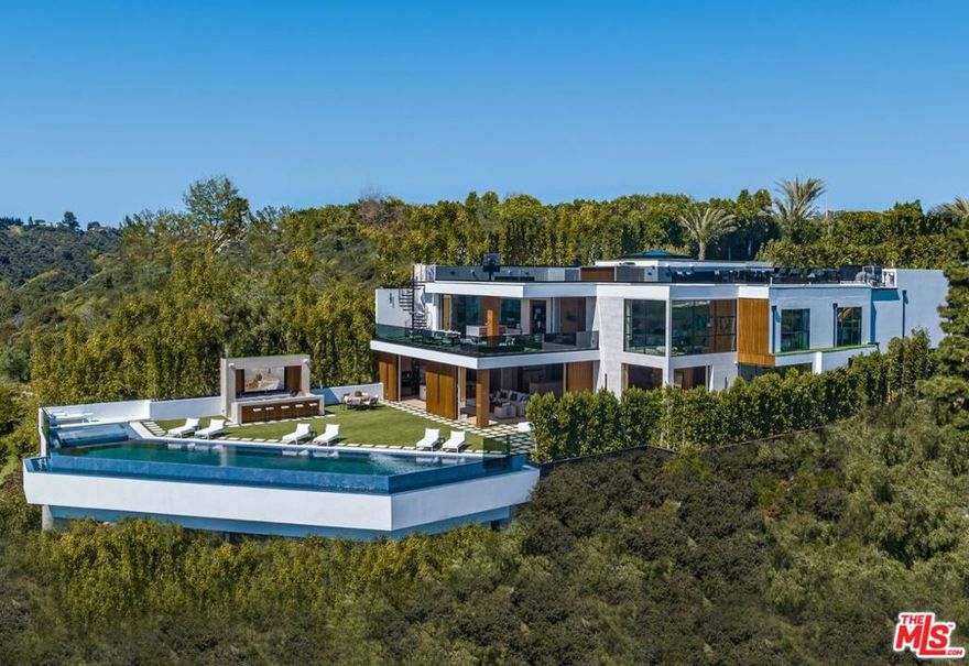 Welcome to Bel-Air Paradise, a brand-new estate, designed and built by the legendary Designer and Developer, Ramtin Ray Nosrati. Descend the private, gated driveway to this incredible oasis set in one of the most prestigious neighborhoods. The lush grounds and gated drive provide the utmost privacy and security. The oversized front door is flanked by walls of glass, wood, and a colorful living wall to create an unforgettable welcome. Step inside to experience the warm contemporary design, high-end finishes, show-stopping living wall, high ceilings, and panoramic ocean/city views. Automated Fleetwood glass doors open throughout the home to create a seamless indoor/outdoor lifestyle. The custom culinary center is a gourmand's dream, with state-of-the-art appliances, adjacent chef's prep area with restaurant-grade walk-in refrigerator, and oversized island. A travertine clad bar and stunning wine room with tasting area help to make this one of the most incredible homes for entertaining. The primary suite is complete with fireplace, wraparound deck with fire pit and sweeping views, spa-inspired bath with oversized rainwater shower, a Zen soaking tub, dual-sink vanity, and custom walk-in closet and dressing room. The latest and greatest amenities include a theater, gym, resort-style tropical landscaping, parking for 7 cars, smart-home system, and automated security. The outdoor oasis offers the perfect space for dining al fresco, outdoor kitchen with bar and flat-screen tv, flat grassy areas, spa, and a massive 80-foot zero-edge infinity-edge pool looking out to incredible city and ocean vistas. There is a large flat area that is perfect for adding a sports court, pickleball court, or tennis court. The outdoor space continues to the rooftop lounge with bar, large tv, fire pit, built-in BBQ, and putting green. Do not miss this opportunity to live at Bel-Air Paradise with jetliner views and incredible amenities in one of the most sought-after locations.