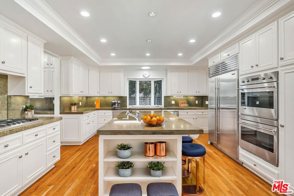 Nestled on a quiet, tree-lined street in the prestigious Beverly Hills Flats, this timeless estate radiates classic elegance and refined charm. Flooded with natural light, the interiors are graced by skylights, vintage details, and sophisticated accents that recall a bygone era of glamour. Set on an expansive, beautifully manicured lot, the residence offers a sprawling grassy yard and enchanting rose garden - an ideal backdrop for both serene mornings and grand entertaining. French doors invite effortless indoor-outdoor living, revealing a covered outdoor kitchen and barbecue pavilion with a cozy fireplace, perfect for year-round gatherings.Beyond its romantic character, the home offers generous living spaces, period architectural touches, and a private, tranquil setting just moments from world-class dining, shopping, and the best of Beverly Hills. Completing this rare offering are a two-car garage and circular motor court with parking for four additional vehicles, as well as a separate guest house perfect for extended stays or private retreats. This estate truly embodies classic Beverly Hills living at its finest.