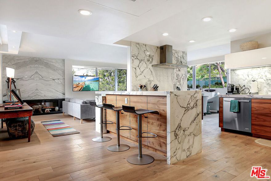 Discover this exquisite 2 bedroom, 2 bathroom condominium at the full service Edgewater Towers perched hillside just 100-yards from the Pacific Ocean. This unit's minimalist design is polished by modern architectural finishes that complement its mid-century roots. Picture windows span opposing walls for natural light and ocean cross breezes to flow, treetop views, and glimpses of the ocean. An open floor plan allows for effortless movement and features hardwood floors throughout, a white marble slab fireplace with black slate hearth in the living room, and a sleek, modern kitchen anchoring the entire space. Rich wood lower cabinets are balanced by the white high gloss uppers, stainless steel appliances, and floor to ceiling white quartz slab countertops and backsplash. The primary bedroom has built-in shelving, walk-in closet, and ensuite bath with slate flooring and glass enclosed double shower and soaking tub. The second bedroom offers beautiful canyon views and ensuite bath. Sip coffee on your private balcony, or enjoy the Edgewater Towers amenities such as basketball and tennis courts, fitness center, heated pool and spa, and 24-hour security. Close to hiking trails, shopping, Will Rogers State Beach, and a quick drive down PCH to Santa Monica or up to Malibu. Second bedroom no longer has built-in desk and murphy bed as shown in photos.