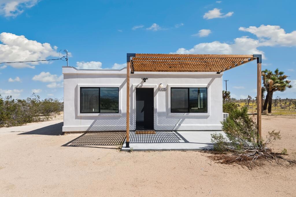 Discover this stylish modernized Spanish-style desert retreat, perfectly set on a fully fenced and gated 5.5+ acre parcel offering privacy, serenity, and endless potential. Turnkey furnished, this home is ready to enjoy as a personal escape, weekend getaway, or investment opportunity. The interior showcases exposed wood beams and a rich wood ceiling, creating warmth and character that blend seamlessly with the desert surroundings. The open floorplan connects the living area and kitchen on one side, with the living room featuring a cozy wood stove and the kitchen highlighted by bold orange cabinetry, induction stove, and mini fridge. The bedroom area includes built-in wood shelving for storage and hanging space, offering both function and charm. The updated bathroom has a vibrant blue tiled shower and skylight. Go outside to a spacious patio for lounging and entertaining, where you can soak in the panoramic desert landscape and breathtaking views in every direction. With plenty of land for expansion or simply to enjoy the peace and quiet, this unique property offers a rare chance to own a private desert hideaway that combines style, comfort, and versatility.