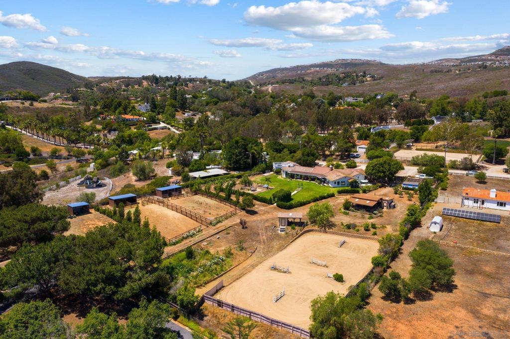 This beautifully maintained 2.51-acre property in Elfin Forest offers a ranch lifestyle with both comfort and functionality. The single-story home features four bedrooms and a flowing floor plan with tasteful upgrades, including an oversized laundry room, open living spaces with a built-in bar area in the family room, and well-appointed bedrooms. Outside, the property is fully equipped for equestrian or livestock use, with a riding arena, 2-stall barn with cross ties and tack room, two fenced pastures with four 12 x 12 shelters, a hay barn, RV parking, and separate access to the backyard amenities. The backyard is a standout feature, with a landscaped archway, mature fruit trees—including banana and mango—garden beds, and a chicken house, all creating a peaceful and productive environment. With privacy, usability, and thoughtful improvements throughout, this is a rare opportunity to enjoy ranch life on the extensive Elfin Forest trail network.