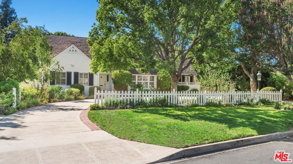 Set on one of Los Angeles' most filmed and picturesque streets, this timeless traditional residence in the sought-after Cameron Woods neighborhood pairs classic charm with expansive living spaces and an entertainer's dream backyard. This single-story estate offers 4BD/2.5BA across a thoughtfully designed floor plan, filled with natural light and warm hardwood floors. The expansive living room welcomes you with a marble fireplace and seamlessly connects to a dining nook with custom built-ins and charming windows. The well-appointed kitchen features a Miele electric cooktop, Sub-Zero refrigerator, and generous counter and cabinet space, complemented by a conveniently located powder room and direct access to the backyard. A versatile bonus living space with rich wood paneling and a second fireplace creates the perfect retreat for a cozy office or family room. Bedrooms are smartly arranged on opposite wings of the home, with the primary suite offering multiple walk-in closets and private access to the patio. A classic entertainment room with a vintage bar, brand new carpeting, and easy outdoor flow further enhances the home's appeal. The backyard is a true private oasis, complete with a covered lanai overlooking a sparkling pool, a built-in stone BBQ, and a detached studio ideal for an office, creative space, or additional storage. The expansive grounds also provide excellent potential for an ADU. Additional highlights include a gated two-car carport and a fully paid, value-enhancing, and money-saving solar energy system. Beyond its charm and functionality, the property also presents unique income potential through film production opportunities. Perfectly situated with convenient access to the 101 and 405 freeways and just moments away from Sherman Oaks Galleria, Costco, and premier dining in Sherman Oaks, this rare offering blends suburban tranquility with city connectivity.