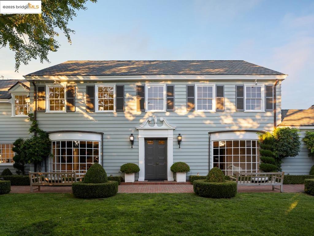 Privately set above the treetops on one of Piedmont’s most storied streets, 120 Hazel Lane is a rare architectural jewel, a stately Colonial estate on an extraordinary ~17,000 sq ft level parcel in the heart of town. Beyond the front gate, its timeless charm recalls the iconic Father of the Bride home. The grand façade is framed by English gardens, pebble paths, and mature landscaping leading to a sun-drenched pool, spa, and storybook cabanas—your own private park. Inside, a curved staircase, hardwood floors, and sunlit rooms flow seamlessly. A mahogany-clad study offers a moody retreat, while the living room with fireplace and oversized windows suits both quiet moments and lively gatherings. The dining room opens to a kitchen/family room with large island, abundant cabinetry, and breakfast nook. A butler’s pantry adds prep space; a main-level bedroom and full bath provide flexibility. French and Dutch doors connect indoors with lush grounds. Upstairs are six bedrooms and four-and-a-half baths, including two en-suites and a serene primary suite with walk-in closet. The third level offers 600+ sq ft of bonus space, and a detached two-car garage completes this amazing once-in-a-generation estate opportunity.