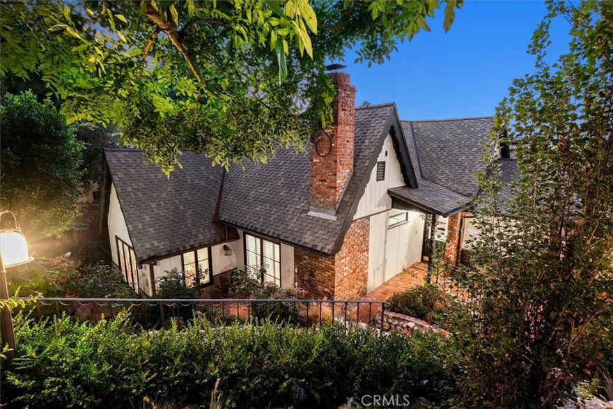 Nestled in the serene hills of Sherman Oaks, this character-rich storybook home is surrounded by lush greenery and offers sweeping mountain and valley views. A winding brick pathway welcomes you to the front entrance, setting the tone for the home’s enchanting appeal. Designed with versatility in mind, the unique two-level floor plan features separate living quarters on each floor. The upper level boasts two bedrooms and two baths, including a spacious primary suite with a luxurious ensuite bath, complete with a soaking tub, romantic fireplace, and a private balcony overlooking breathtaking vistas. The living room showcases high wood-beamed ceilings and a charming brick fireplace, while the formal dining room and chef’s kitchen with top of the line appliances, provide the perfect setting for entertaining. The lower level offers a flexible one-bedroom/den layout, a beautifully remodeled kitchen, and a classic brick wine cellar. Step outside to discover multiple brick patios, a private grassy yard, a built-in pizza oven and a delightful rose garden ideal for relaxing or hosting under the California sun. The garage boasts a second story that is great for storage. Though this tranquil retreat feels worlds away, it’s just minutes from the vibrant shops, fine dining, and all the wonderful conveniences of Ventura Boulevard and the heart of Sherman Oaks.