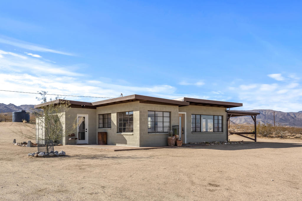 This stunning mid-century home, situated on a breathtaking 5-acre property, offering a perfect blend of modern comfort and timeless desert charm. Designed with clean lines, large windows, and open-concept layout, that seamlessly integrates indoor and outdoor living. Expansive casement windows frame sweeping views of the rugged Mojave landscape, from rolling desert hills to distant mountains painted in golden hues at sunset. The interior features a minimalist ranch aesthetic that enhances the home's architectural elegance. A spacious living area opens to a chef's kitchen, complete with sleek cabinetry, stainless steel appliances, kitchen dining area and bar top. The bedroom is serene, with casement windows that let in soft natural light and offer uninterrupted views of the vast desert sky. Outside, a sprawling shaded lounge area creates an ideal space for stargazing or soaking in the peaceful solitude of the high desert. This mid-century gem captures the magic of desert living-where design meets the untamed beauty of the California wilderness. Home has been verified by SB County as a STR property if you decide to apply for permit. Expand another 5 acres to the adjacent parcel currently for sale.