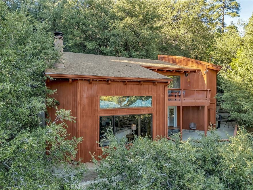 Sited high above the street in the quiet Cedar Glen neighborhood, this warm and inviting mountain home is surrounded by towering pines, dramatic boulders, and a peaceful sense of retreat. Thoughtfully remodeled and designed for comfort, the main level welcomes you with an open living space anchored by a striking floor to ceiling rock fireplace crafted with sculpted manzanita branches. Vaulted ceilings and large windows fill the room with soft natural light, creating a true treetop atmosphere. The living, dining, and kitchen areas blend together with an easy, connected flow. The kitchen features custom cabinetry, quartz counters, stainless appliances, and a breakfast bar perfect for casual meals or gathering with friends. Stained glass windows facing southeast add warmth, color, and morning glow to the space. A comfortable bedroom and bath on this level allow for simple single level living, and the main deck offers an ideal spot for relaxing in the forest setting. A spiral staircase leads to the upper floor, where the home opens into several flexible, welcoming spaces. A generous game room with a wet bar offers an enjoyable area for entertaining or weekend fun. Just beyond, a secluded sitting area provides a peaceful space for a home office, reading nook, or additional sleeping area as needed. This sitting area opens to a private front deck perched above the trees. The upstairs bedroom enjoys direct access to the expansive backyard patio, framed by pines and natural rock formations, and offers convenient access to the upper parking area from Highway 243. The upper level also features a spa like bath with custom tilework and a spacious tub and shower, creating a calm and restorative place to unwind. A small sleeping loft, accessed by ladder, adds a charming option for guests. The property includes a cargo lift that carries items from the lowest point of the property to the highest, providing practical support for transporting groceries, wood, or supplies. Multiple outdoor living areas, including decks and a large patio, offer a variety of places to enjoy the mountain air. The adjacent .33 acre parcel is also available for purchase, offering natural boulders, mature pines, and potential access from Highway 243. Located near the Nature Center and miles of hiking trails, and just minutes from town, this Cedar Glen home offers an elevated mountain experience with comfort, privacy, and room to gather.