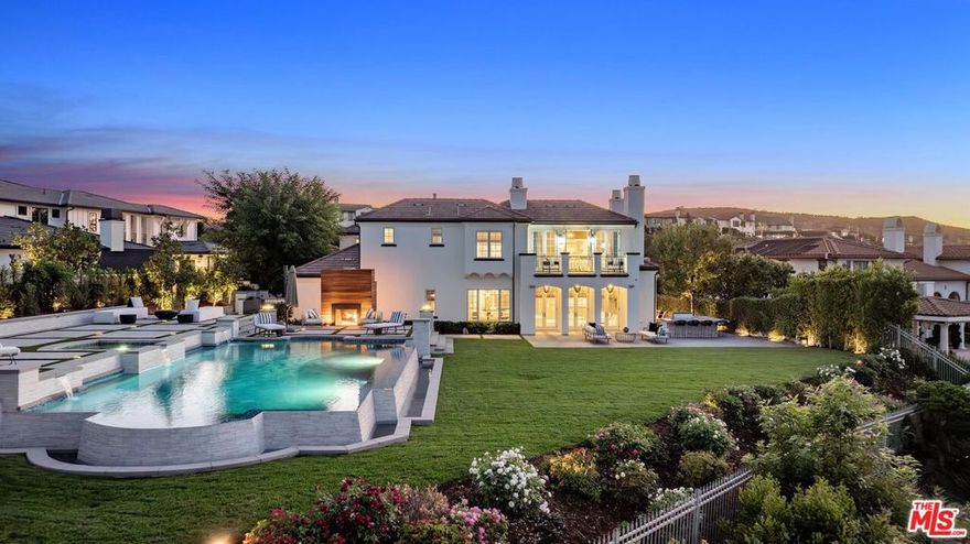 Welcome to this beautifully upgraded Classics Plan 3 home situated in The Oaks of Calabasas, one of Southern California's most prestigious guard gated communities. This exceptional two-story, 5BD/5.5BA estate combines timeless architecture with modern luxury, offering refined interiors, smart home upgrades, and panoramic views. Inside, warm hardwood floors, arched hallways, and custom details create an inviting atmosphere. Just off the entry, a sophisticated office with built-in cabinetry and expansive windows provides a serene space for work or study. The first ensuite bedroom is located downstairs, as well as a powder bath conveniently located near the entryway for guests. Down the hallway, the formal living room features an elegant fireplace, creating a cozy yet elevated setting. It flows seamlessly into the formal dining room, anchored by a statement chandelier and french doors extending the space to a charming outdoor seating area. At the heart of the home lies the expansive family room, distinguished by high ceilings, exposed wooden beams, and a second fireplace that adds rustic charm to the sophisticated design. This space opens directly to the gourmet kitchen, where a dramatic quartzite center island, high-end appliances, and abundant cabinetry create the ideal space for both everyday living and entertaining. A butler's pantry connects the dining room to the kitchen, enhancing both functionality and flow. Upstairs, a versatile bonus room awaits, adorned with barn doors and a drop-down movie screen, perfect for a media lounge or playroom. The primary suite is a true retreat, featuring a private balcony that captures the backyard and picturesque hills, a spacious bonus room ideal for a gym, nursery, or office, a walk-in closet, and a luxurious ensuite bath. The spa-inspired bathroom includes a freestanding soaking tub positioned to take in scenic views, dual vanities and an expansive steam shower. Three additional ensuite bedrooms offer ample closet space and privacy, while a dedicated laundry room on this level adds convenience. The resort-style backyard offers an infinity-edge pool and spa with fountains, lush landscaping, a built-in barbecue and fridge, outdoor speakers, and a dual fireplace creating multiple zones for lounging, dining, and entertaining, all set against a backdrop of breathtaking views. As a resident of The Oaks of Calabasas, you'll enjoy 24-hour gated security and proximity to nature trails, top-rated schools, and premier shopping and dining destinations. Welcome to a new standard of luxury living!