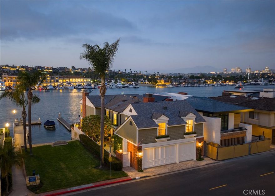 Positioned on a rare 40-foot wide parcel along one of Lido Isle’s most desirable waterfront stretches, this bayfront residence offers an uncommon combination of scale, proportion, and orientation. Designed in a traditional style and executed with architectural clarity, the home encompasses nearly 4,000 square feet of interior space with uninterrupted views across one of the harbor’s broadest channels. The site adjoins a private park and sandy beach, affording both visual breadth and lateral privacy—attributes not oft found on this private island. The layout is structured to accommodate both formal and informal living. Principal rooms, including a well-composed living room and a dining area of considerable dimension, open to broad waterside terraces. The kitchen, positioned to capture views of the bay, is paired with a casual dining area and an adjacent family room. A discreet guest bath completes the main level. Above, the primary suite occupies a substantial portion of the upper floor and includes a private water-view sitting area with fireplace, a sleeping room with water and city-light vistas as well as a private terrace, a bath clad in Italian marble, and a dressing area of considerable scale. Two secondary bedrooms share a full bath, completing the private quarters. A commercial-grade elevator serves all levels, offering both practicality and ease. The three-car garage includes additional storage, while the private dock accommodates a sizable vessel and is complemented by a waterside pier patio—designed for comfortable living at the water's edge. This home's location is but steps from the island's private beaches, tennis courts, many parks, and clubhouse. Restrained, elegant, and offered in perfect condition, this residence offers a rare opportunity to enjoy the very best of Lido Isle.