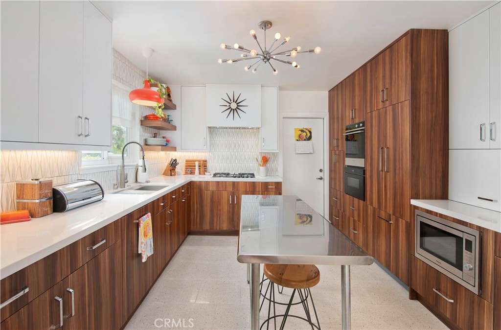 Step into timeless design and effortless living in this beautifully upgraded 4-bedroom, 2-bath mid-century gem, ideally situated on a tree-lined street in the highly sought-after Rolling Greens neighborhood of Granada Hills. Spanning 1,795 sq ft, this single-story residence seamlessly blends iconic mid-century architecture with clean, modern Scandinavian style—offering crisp lines, refined functionality, and sun-drenched, open living spaces. At the heart of the home lies a striking Scandinavian-inspired kitchen designed with minimalist flair. It features sleek custom cabinetry, natural wood accents, terrazzo flooring, and high-end Fisher & Paykel appliances including a luxury cooktop and oven. Hidden panel-front refrigerator and dishwasher complete the look, preserving the kitchen’s seamless and sophisticated aesthetic. The open-concept design flows effortlessly into the dining area and expansive living room, where vaulted beam ceilings and generous windows enhance the light and airy ambiance—ideal for both relaxed living and stylish entertaining. The thoughtfully designed floor plan includes a private hallway leading to the oversized primary suite—an inviting retreat with ample windows and French doors that open directly to the serene backyard. The spa-like primary bath offers a calming escape, complete with a soaking tub perfectly positioned beneath a skylight, a separate walk-in shower, and luxurious finishes throughout. Three additional bedrooms provide comfortable versatility, each filled with natural light. One of the secondary bedrooms features its own French doors opening to a peaceful side patio—perfect for a guest room, home office, or creative studio. Both bathrooms have been tastefully remodeled to reflect the home’s sleek, modern aesthetic. Step outside and enjoy multiple spaces for outdoor entertaining, from the covered patios to a dedicated play area, artificial turf, and beautifully landscaped drought-tolerant gardens that create a private, low-maintenance oasis. No detail has been overlooked in this masterfully curated home—featuring rich Acacia wood flooring, recessed lighting, newer roof, upgraded electrical panel, updated HVAC, Owned solar panels, EV charger and more. This is a rare opportunity to own a truly special Mid-Century Modern home in one of Granada Hills’ most coveted enclaves.