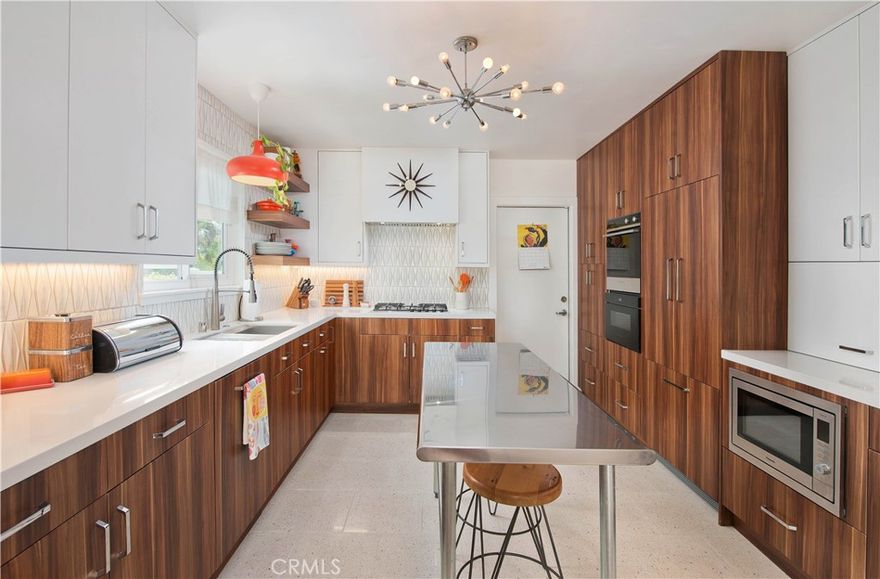 Step into timeless design and effortless living in this beautifully upgraded 4-bedroom, 2-bath mid-century gem, ideally situated on a tree-lined street in the highly sought-after Rolling Greens neighborhood of Granada Hills. Spanning 1,795 sq ft, this single-story residence seamlessly blends iconic mid-century architecture with clean, modern Scandinavian style—offering crisp lines, refined functionality, and sun-drenched, open living spaces. At the heart of the home lies a striking Scandinavian-inspired kitchen designed with minimalist flair. It features sleek custom cabinetry, natural wood accents, terrazzo flooring, and high-end Fisher & Paykel appliances including a luxury cooktop and oven. Hidden panel-front refrigerator and dishwasher complete the look, preserving the kitchen’s seamless and sophisticated aesthetic. The open-concept design flows effortlessly into the dining area and expansive living room, where vaulted beam ceilings and generous windows enhance the light and airy ambiance—ideal for both relaxed living and stylish entertaining. The thoughtfully designed floor plan includes a private hallway leading to the oversized primary suite—an inviting retreat with ample windows and French doors that open directly to the serene backyard. The spa-like primary bath offers a calming escape, complete with a soaking tub perfectly positioned beneath a skylight, a separate walk-in shower, and luxurious finishes throughout. Three additional bedrooms provide comfortable versatility, each filled with natural light. One of the secondary bedrooms features its own French doors opening to a peaceful side patio—perfect for a guest room, home office, or creative studio. Both bathrooms have been tastefully remodeled to reflect the home’s sleek, modern aesthetic. Step outside and enjoy multiple spaces for outdoor entertaining, from the covered patios to a dedicated play area, artificial turf, and beautifully landscaped drought-tolerant gardens that create a private, low-maintenance oasis. No detail has been overlooked in this masterfully curated home—featuring rich Acacia wood flooring, recessed lighting, newer roof, upgraded electrical panel, updated HVAC, Owned solar panels, EV charger and more. This is a rare opportunity to own a truly special Mid-Century Modern home in one of Granada Hills’ most coveted enclaves.