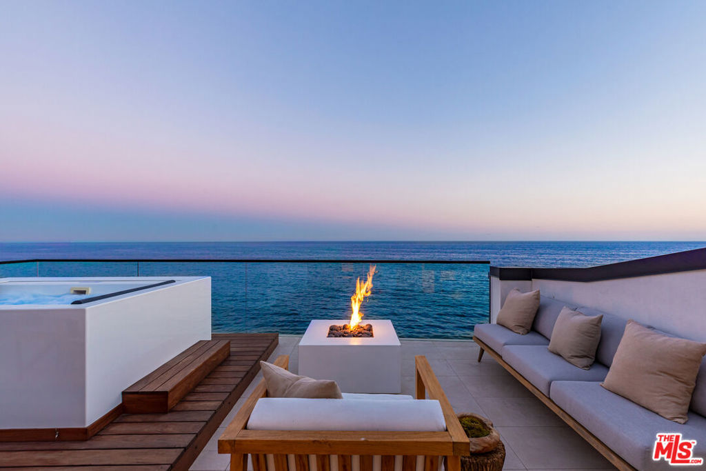 From the vanishing glass walls to the enormous oceanfront decks to the rooftop lounge and spa, this sensational new home is contemporary beachfront living at its finest. Completed in 2022 with steel-frame construction and smart-home amenities, the property's custom design forefronts amazing views and exceptional comfort. Approximately 57 feet of beach frontage faces onto the ocean, islands, and the sparkling Queen's Necklace from a very convenient location close to both Santa Monica and the Malibu Country Mart. The main floor comprises an open-plan living/dining/kitchen great room with unobstructed views. Sleek finishes include an ultra-modern fireplace, a wine storage display, wraparound windows, and a wall of Fleetwood doors that opens fully to extend the space to a large outdoor living and dining deck overlooking the sea. The kitchen features a huge stone-top island with bar seating, handsome custom cabinets, and top-of-the-line Miele appliances. On the upper floor, accessed by a gorgeous wood staircase with mountain views, the three bedrooms are each customized with wide-plank walnut flooring, closets with Italian leather shelves, and bathrooms of natural limestone. The primary suite is a breathtaking retreat with double-height ceilings, a fireplace, a yoga/office loft, an enormous oceanfront deck, and a truly inspired spa-style bath. Completing this already exquisite residence is a rooftop deck for lounging and entertaining. Equipped with marine-grade appliances and wraparound views, the deck features a modern hot tub, a fire pit, and ample room for dining, entertaining, and lounging, day and night. The home's many up-to-the-minute amenities include automated window shades throughout, plus a private stairway to the sandy beach. With its blend of modernist design and majestic setting, this outstanding residence offers a lifestyle of harmony and luxury.