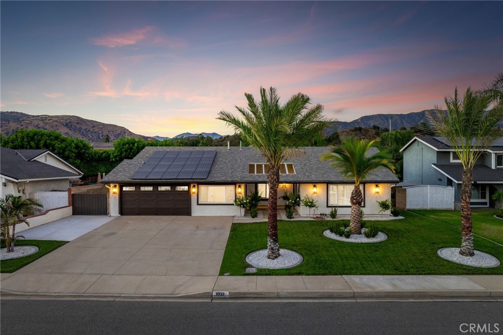 Reimagined and redesigned, this home showcases a true open-concept floor plan with soaring ceilings and a 15-foot multi-panel folding glass door framing panoramic views of the backyard and pool. The front yard offers clean curb appeal with a manicured lawn, mature date palms, planters, RV parking, and a welcoming courtyard leading to double arched iron entry doors. Inside, this virtually brand-new residence features wide-plank hardwood flooring, plantation-shuttered windows, a living room overlooking the front yard, an adjacent dining area, and a center-positioned kitchen. The kitchen is a showpiece with custom wood cabinetry, quartz countertops and backsplash, a center island with pendant lighting and seating, plus a separate buffet with a wine fridge and added storage. The adjoining family room highlights a modern linear gas fireplace, a flush-mounted 85” TV, and the expansive folding glass doors that flood the space with natural light and provide seamless indoor-outdoor living. The primary suite, accessed through double doors, features LED lighting, mirrored closet doors, and shuttered windows with backyard views. Its custom bath offers dual sinks with marble counters, gold fixtures, a frameless glass marble shower, and a striking marble accent wall. Three additional bedrooms, a remodeled hall bath, and a finished laundry room with cabinetry and counter space complete the interior. Additional upgrades include new interior doors and hardware, new HVAC system with ducting, and a leased solar system. Outdoors, the backyard is designed for entertaining with a pool and spa, a large grassy area, expansive decking, block perimeter walls, and rear planters with queen palms and ficus trees that will grow into a lush privacy hedge. The side yard features gated, fully concreted RV parking.