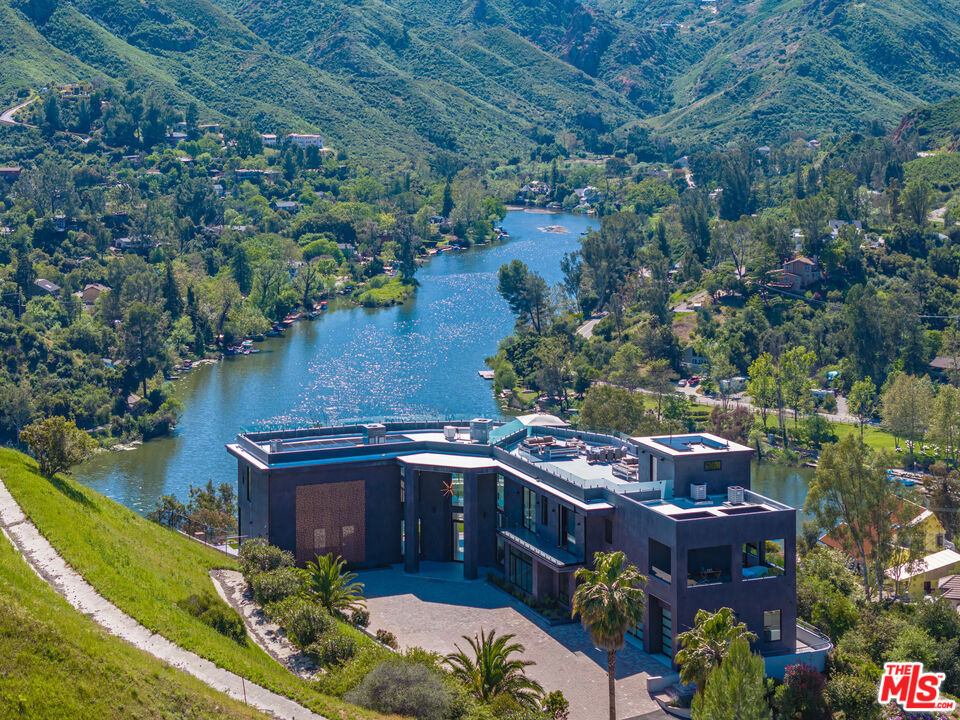 Introducing an architectural marvel boasting unparalleled panoramic views that redefines luxury living in Southern California. Crafted by GoDesign21, this European Contemporary spans over 6,500 sq ft with meticulous attention to detail. Situated in Malibou Lake, it offers complete privacy atop 3.41 acres, accessed via a private 400-foot driveway. Enter through the impressive glass pivot door into an open-concept floor plan, seamlessly blending indoor and outdoor spaces. The interior features soaring ceilings, sliding doors, a wine wall, and a screening room. The chef's kitchen boasts Leicht German Cabinetry, quartz countertops, top-tier Miele appliances, and a butlers pantry. The primary suite offers two walk-in closets, a fireplace, balcony, and a spa-like bathroom. Additional highlights include en-suite bedrooms, an indoor/outdoor gym, and bespoke finishes. Outside, an infinity pool, outdoor kitchen, landscaped grounds and over 1,700 sq. ft. rooftop with captivating views. Equipped with smart home tech, security cameras, solar, audio speakers, and Spanish Oak floors. Close to the 101, shopping, dining, and Malibu, this property epitomizes luxury living in an unrivaled setting.