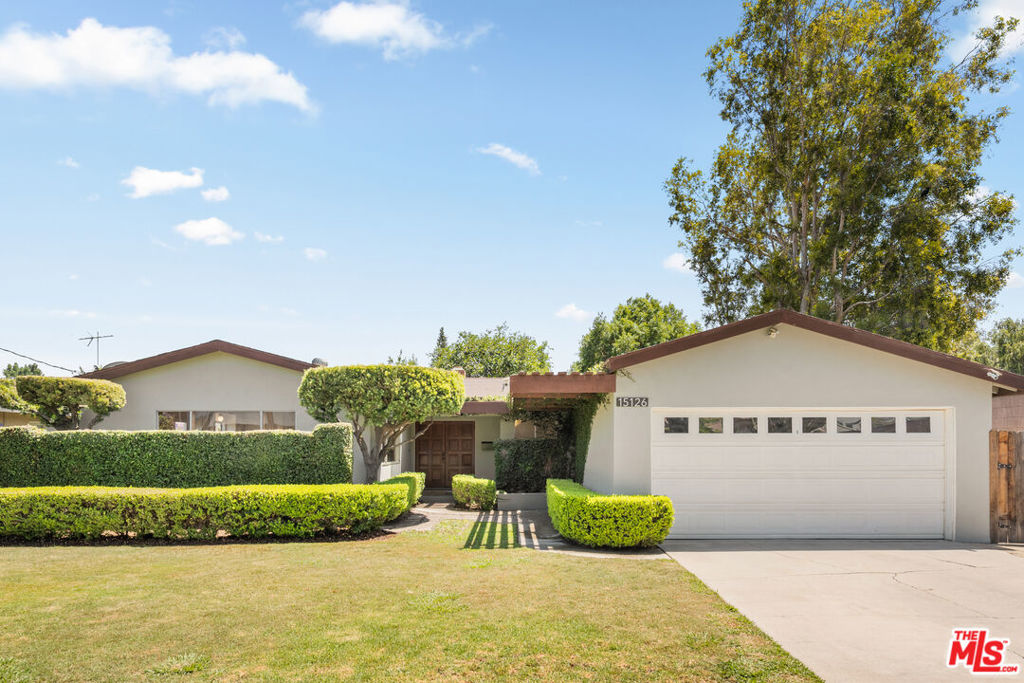 Tucked away on a quiet cul-de-sac, 15126 Archwood offers timeless mid-century charm on an expansive lot designed for both privacy and possibility. This move-in ready residence blends classic style with thoughtful updates, featuring large bedrooms and light-filled living spaces that create a warm and welcoming atmosphere. Step through double wood doors into a home where original character meets modern comfort. Refinished hardwood oak floors flow through the kitchen and family room where wood-paneled walls echo the home's mid-century roots. The living room boasts clay tile flooring and a striking stone fireplace. Recessed lighting, new fixtures, and refreshed bathrooms and kitchen enhance the home's livability with tasteful, modern touches. The spacious primary suite offers direct access to the patio and backyard, along with a double vanity bathroom for added convenience. Outdoors, a large, private backyard beckons with mature Melogold grapefruit and Hachiya persimmon trees and ample room to add a pool or create a garden retreat. Retro breeze block walls draped in vines provide stylish seclusion at the front. Complete with a two-car garage and abundant natural light throughout, this is a rare opportunity to own a home that blends vintage appeal with today's essentialsall in a serene, sought-after setting.