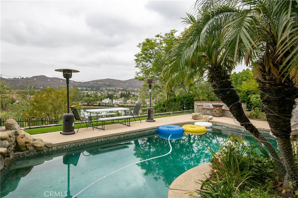Stunning Wood Ranch Pool Home with Panoramic Views and Resort-Style Amenities. Welcome to this spacious 5-bed, 3-bath pool home on a generous lot in the highly sought-after Wood Ranch community. With over 3,300 sq ft of refined living space, this entertainer’s dream offers sweeping views of the hills and a tranquil private lake—accessible only to residents through a gated entry. Neighborhood security patrol provides added peace of mind. Enjoy the scenery from the private master balcony or the beautifully landscaped backyard with multiple seating areas and lush surroundings. Inside, a dramatic entryway features a sweeping staircase and soaring ceilings. Elegant living and dining rooms each include cozy gas fireplaces—part of a total of four fireplaces throughout the home. The formal dining room opens to a patio and outdoor kitchen, creating seamless indoor-outdoor flow. The chef’s kitchen features granite countertops, custom stone finishes, Sub-Zero fridge, Miele dishwasher, double ovens, 6-burner Wolf range, and a large walk-in pantry. A center island and breakfast nook open to a spacious family room with another fireplace and direct access to the pool. A downstairs bedroom and full bath make a perfect guest suite. Upstairs, the luxurious primary suite includes its own fireplace, dual walk-in closets, and a spa-like bath with Jacuzzi tub and steam shower. Enjoy lake and hillside views from the private balcony. Three additional bedrooms—one with built-ins and its own fireplace—offer flexible space for family or home office use. The resort-style backyard features a pool and spa, built-in outdoor kitchen with BBQ, fridge, sink, dining area, fire pit, and more. A solar power system adds energy efficiency and savings. Residents enjoy private access to a nearby park with tennis, volleyball, and basketball courts, plus close proximity to Rancho Madera Park, Wood Ranch Golf Club, hiking trails, and the Reagan Library. Luxury, lifestyle, and location—this home has it all.