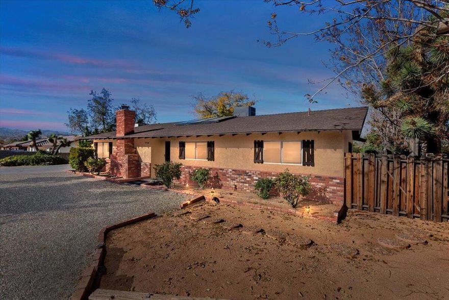 Discover this exceptionally charming home tucked away in the highly desirable Western Hills Ranchos neighborhood. Located on a peaceful cul-de-sac, this spacious property offers a welcoming blend of character, comfort, and potential both inside and out.Step into a massive living room featuring a beautiful wooden accent wall, lovely new flooring, and a cozy fireplace that sets the tone for the home's inviting feel. The layout includes a separate dining room and a fully remodeled kitchen showcasing an apron sink, quartz countertops, shaker cabinets, and updated finishes throughout. This bright and stylish kitchen connects directly to the home's standout feature: an expansive sunroom.Filled with natural light from multiple skylights and open windows, the sunroom offers surrounding views of the lush backyard and provides access to the kitchen, outdoors, and primary bedroom. It also has the potential to be converted into additional living space or extra rooms if desired.The primary suite includes a walk-in closet, a jetted Jacuzzi tub, dual sinks, a built-in vanity, and private access to the sunroom. Both bathrooms are generously sized, complementing the home's comfortable, family-friendly layout.Outdoors, you'll find one of the most unique and beloved features of the property: a beautifully maintained garden oasis with mature trees, grapevines, and real grass. This rare, lush setting creates the feeling of not even being in the desert. Multiple gated entry points, a built-in outdoor barbecue area, patio seating, and charming landscaping make the backyard perfect for entertaining or relaxing in total privacy.The home also features newer HVAC, sewer connection, two large driveways that both provide access to the house (one with a full wraparound), an outdoor shed for additional storage, and an oversized garage with plentiful space that could also be converted into additional bedrooms. It was previously used as an art studio.With its warm, homey feel, spacious layout, and highly usable yard, this property is ideal as a family home, a desert retreat, or a strong investment opportunity. A must-see in one of Yucca Valley's most sought-after neighborhoods.