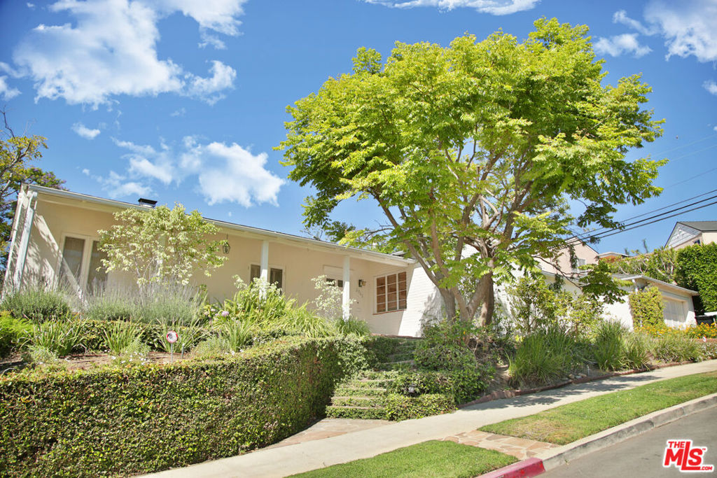 Nestled on one of the most picturesque streets in Cheviot Hills, this warm and welcoming single-story home offers timeless appeal, character, and a layout that's as functional as it is inviting. Set on a sprawling corner lot, the home features a sun-filled living room with vaulted ceilings, a classic marble fireplace, custom built-ins, and a large picture window that frames views of the beautifully landscaped front garden. Just off the living room, a gracious formal dining room opens to the outdoors through French doors and includes a wood-accented wet bar, perfect for entertaining. The private, grassy yard and charming covered patio create an ideal backdrop for morning coffee, or relaxed evenings under the stars.Inside, you'll find three spacious bedrooms and three bathrooms, along with a richly paneled den that easily functions as a home office or fourth bedroom. A separate bonus room offers flexible space for a creative studio. Thoughtful architectural details and original charm carry throughout the home, seamlessly connecting the inviting interiors with the lush outdoor spaces. From the rolling green lawn to the mature trees and vibrant landscaping, every element reflects a home that's been lovingly cared for and truly cherished.