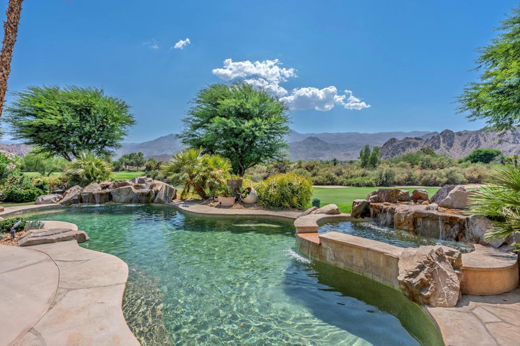 Located on the prestigious Jack Nicklaus Private Course in PGA West, this home is positioned on the 16th fairway with expansive double fairway views and no homes across the fairway, creating an unparalleled sense of openness and privacy. From the moment you enter, you're greeted by walls of glass framing the incredible views and a dramatic living room fireplace that serves as a striking focal point. The interior showcases top-tier finishes throughout, including wood-paneled ceilings, solid core wood doors, custom front door, wood-framed windows, custom baseboards, motorized window coverings, and custom lighting fixtures that exude sophistication and craftsmanship. The chef's kitchen is equipped with Wolf cooktop and Thermador appliances, a SubZero refrigerator, GE Monogram wine fridge, and custom cabinetry, blending function and luxury seamlessly. Each bedroom is en suite, and the private casita features a built-in office. Outdoor living is enhanced by misters, cascading water features, retractable awnings, a water fountain, BBQ area, and beautifully paved courtyard and front yard, designed for comfort and style. The epoxy-finished two-car garage + golf cart gives you plenty of room. A recently installed air conditioner adds convenience and peace of mind. This home embodies the finest that PGA West has to offer. This unique location is a neighborhood favorite and one you don't want to miss. If you appreciate high quality finishes you will not be disappointed here. Set up a private showing and see this home in person today.
