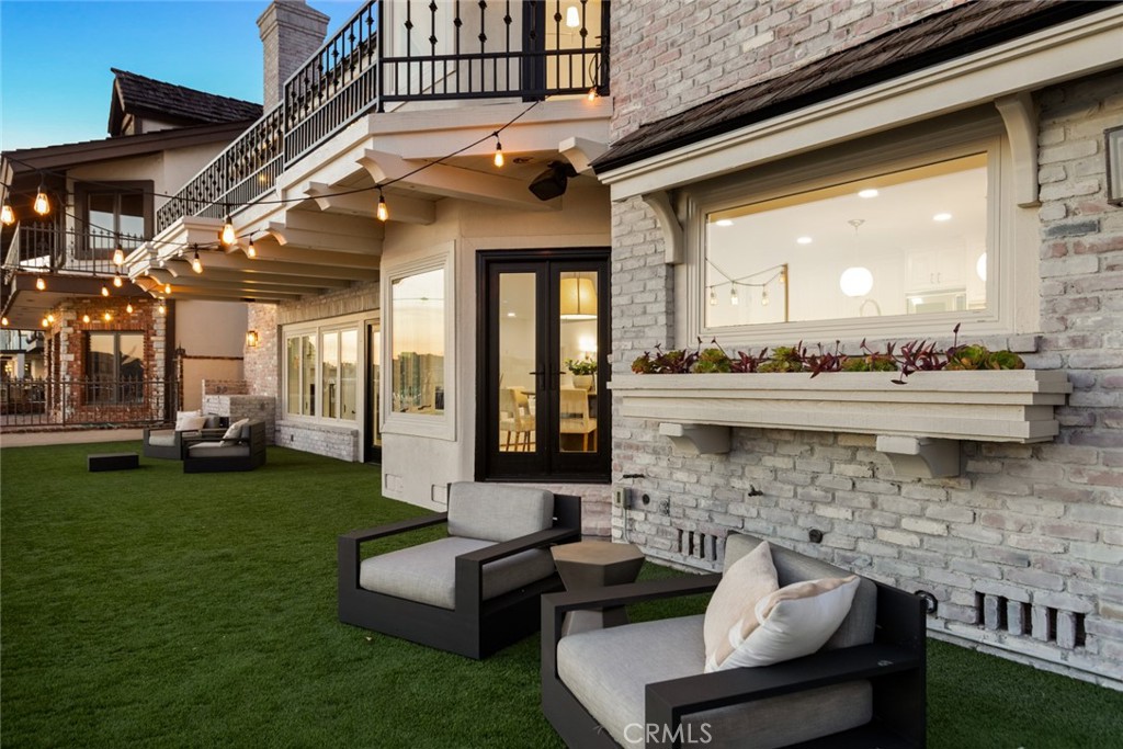 With a premium waterfront setting on Trinidad Island overlooking Huntington Harbour’s main channel, this extensively upgraded home redefines luxury living in Southern California. A covered entry porch and a gated driveway enrich the undeniable curb appeal of the residence and complement its elegant Tudor-style architecture, distinguished by whitewashed brick and prominent dormer windows. Leaded-glass windows and sidelites embellish the front door, creating a warm introduction to living areas that extend approximately 5,000 square feet. Discover four ensuite bedrooms, five baths, a dramatic two-story foyer with circular staircase, a fireplace-warmed formal living room with bay window and vaulted ceiling with beams, and a sophisticated formal dining room with bay window, contemporary chandelier, corner cabinets with glass display shelves, and a handsome tray ceiling. Watch sailboats glide by while relaxing in an large family room with corner fireplace and seamless access to a casual breakfast nook with bay window and backyard access. Anchored by an oversized island and enhanced with harbor views, the kitchen showcases a mix of black and white stone countertops, custom wood cabinetry, walk-in pantry, top-tier Thermador and Viking appliances, cabinet matched Sub-Zero refrigerator, prep sink and fixtures shining with unlacquered brass. One ensuite bedroom is currently featured as a home office on the first level, and two other ensuite secondary bedrooms are offered upstairs. Crowned by a third-level turret-style viewing room with wet bar, the opulent primary suite is sequestered beyond double doors and reveals a fireplace, sitting area, a large balcony with panoramic harbor, sunset and evening-light views, a walk-in closet with built-ins, and a freestanding soaking tub. For the ultimate in entertaining, this grand residence boasts a massive bonus room with wet bar, pool table and bathroom. Upgrades are led by hardwood flooring, designer lighting fixtures, custom millwork including crown molding and judges paneling, recessed LED lighting, and custom stone fireplace surrounds. The bayfront backyard offers ample space for enjoyment, and yacht enthusiasts are accommodated by two private boat slips that can house vessels up to 46’. Trinidad Island is home to a beachfront park, waterfront pathways and scenic paseos, enhancing the idyllic Huntington Harbour lifestyle.