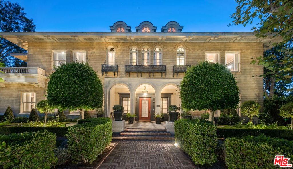 Modern luxury meets timeless elegance in this fully restored Hancock Park estate, designed in 1914 by iconic architects Hunt & Burns for Milton Getz, president of Sun Drug Company. Beautifully reenvisioned by Bowery Design Group, the residence evokes the glamour of The Great Gatsby, reimagined for today. The dramatic two-story entry showcases original windows, moldings, wainscoting, and built-ins. The main level includes a formal living and dining room, a vintage game room, and an entertainer's kitchen with a Theramador range, dual refrigerators, and three Miele dishwashers. Upstairs, the primary suite offers a spa-like bath, custom closets, and 2 private terraces. 4 additional bedrooms complete the floor. The 3rd level serves as a retreat for guests or children with a living room, 2 bedrooms, and a bath. The lower entertainment level features a speakeasy, cigar lounge, theater, gym, and second laundry room. Outside, landscaped grounds ensure privacy with mature trees and a secured gated drive. Amenities include a 3-car garage with guest house above, pool and spa, outdoor kitchen and bar, cabana with fireplace, fire pit, EV charger, water softener, backup generator, and security camera system. A rare architectural icon in Hancock Park, restored and reimagined for modern living and entertaining.